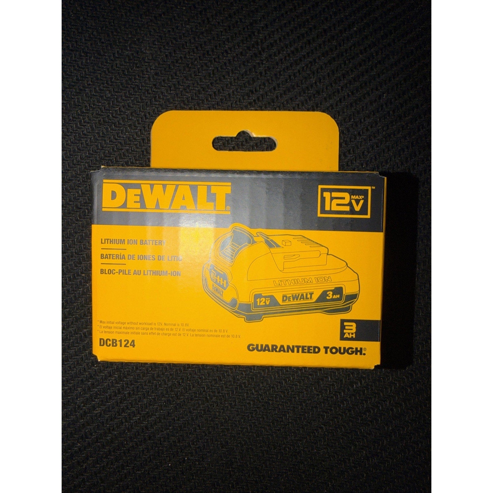 Yellow and black DEWALT 12V 3Ah lithium ion battery packaging with product illustration, model number DCB124, and "Guaranteed Tough" slogan on a dark textured surface.