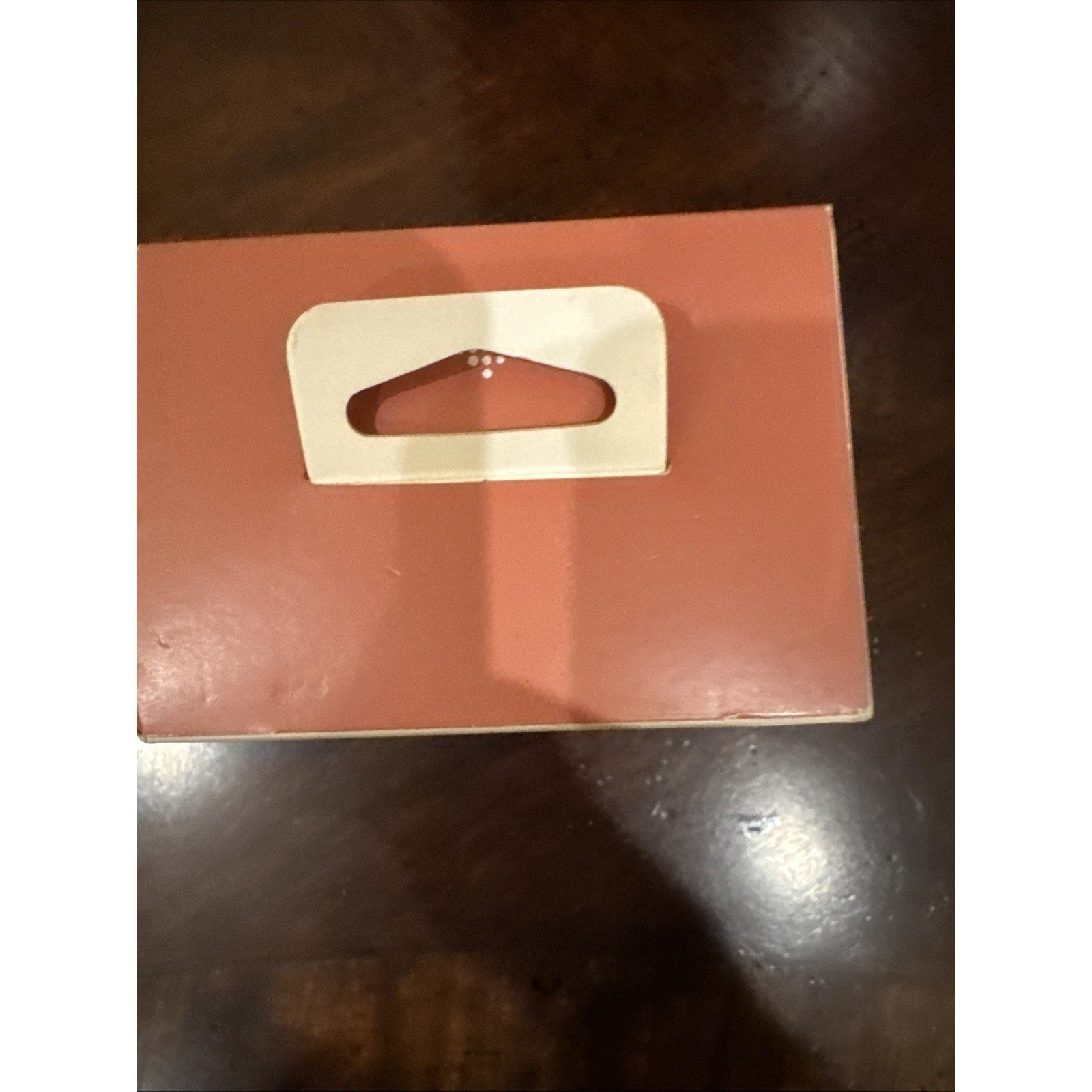 Top view of pink sand Fitbit Versa 4 smartwatch box with white hanging tab on brown surface