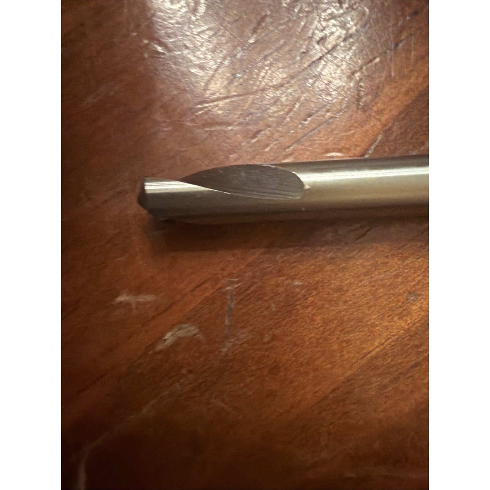 Close-up of a metal cutting or drilling tool with a smooth cylindrical shank and a rounded cutting tip, resting on a wooden surface with visible grain and scratches.