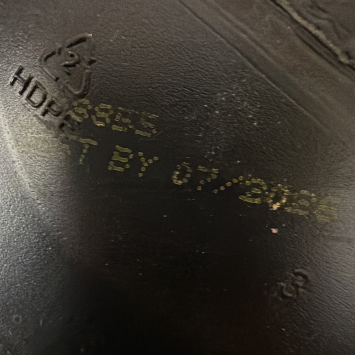 Close-up of a black plastic surface with embossed recycling symbol and faded yellow printed text showing a best-by date of 07/2025.