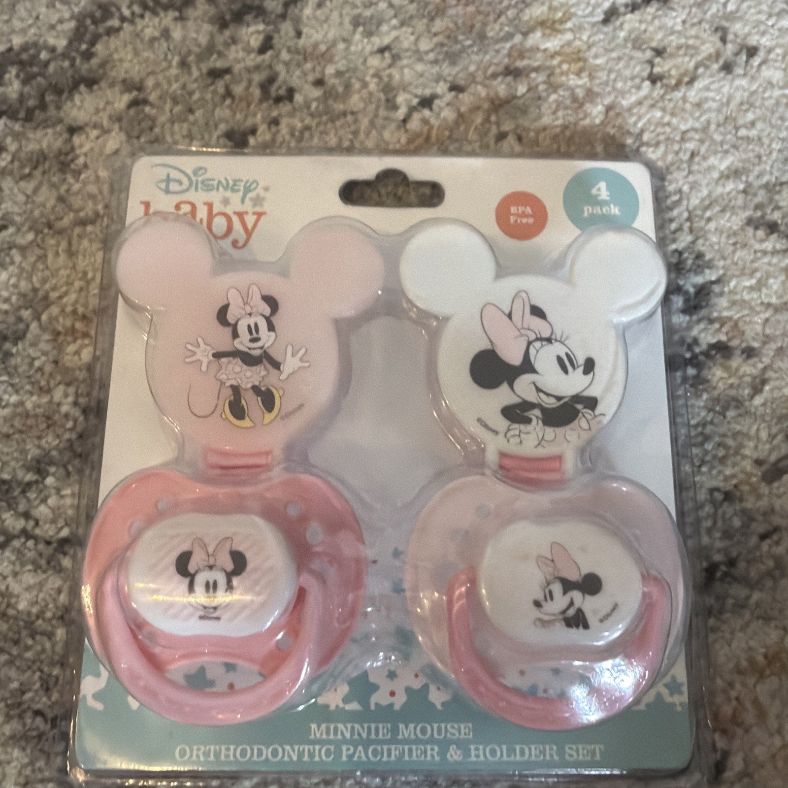 Set of two Disney Baby Minnie Mouse orthodontic pacifiers with pink handles and matching holders shaped like Minnie Mouse’s head, packaged in a clear plastic and cardboard backing.