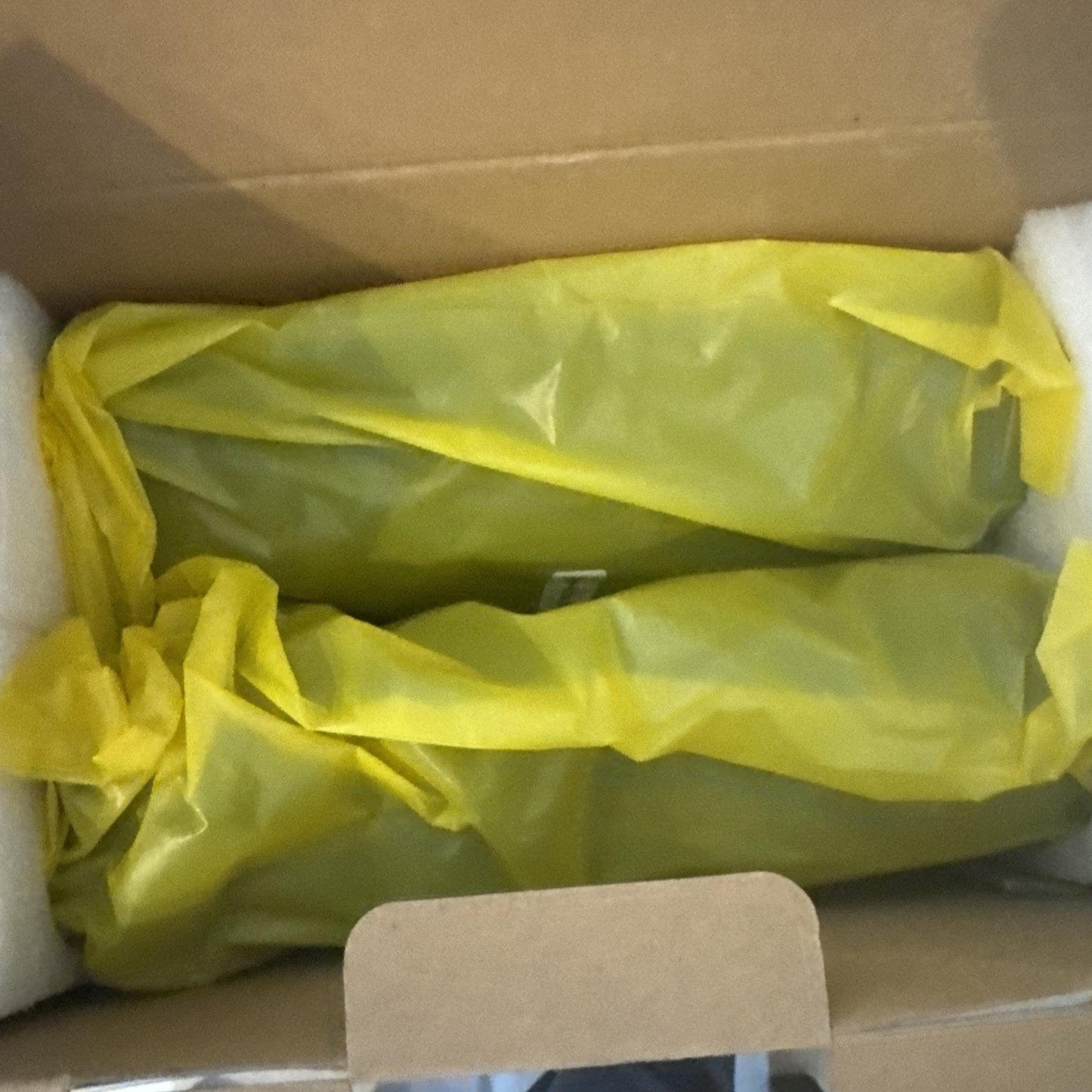 Two items wrapped in yellow plastic placed inside a cardboard box with white foam padding on the sides for protection.