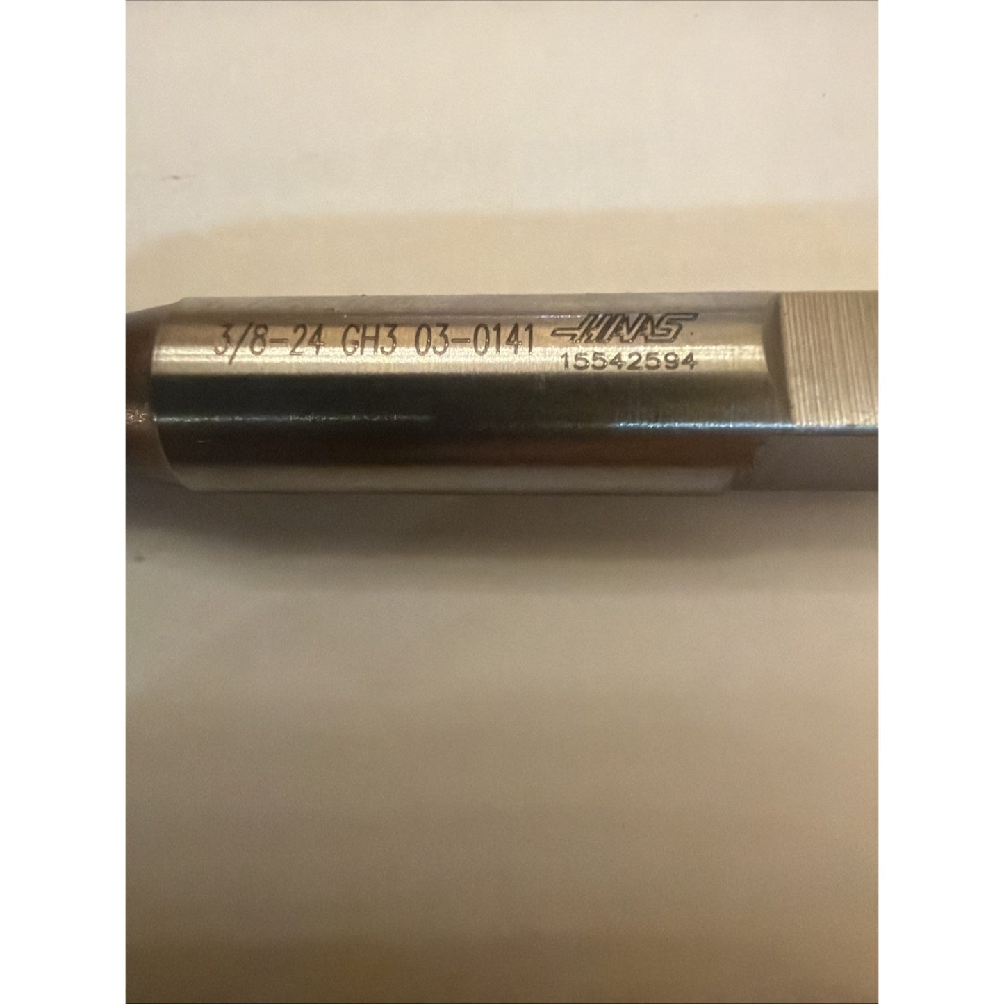 Close-up of a cylindrical metal threading tool with engraved alphanumeric markings and a brand logo, resting horizontally on a light-colored surface.