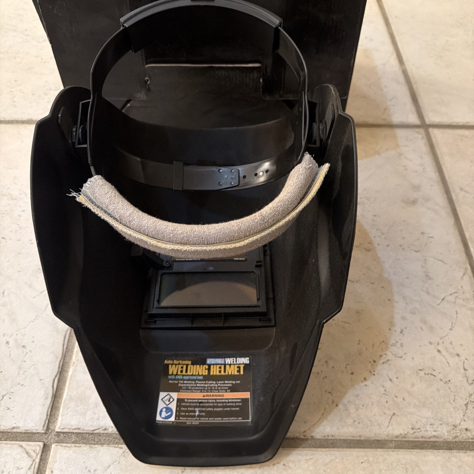 Chicago Electric auto-darkening welding helmet with adjustable shade and black plastic shell shown open on tiled floor