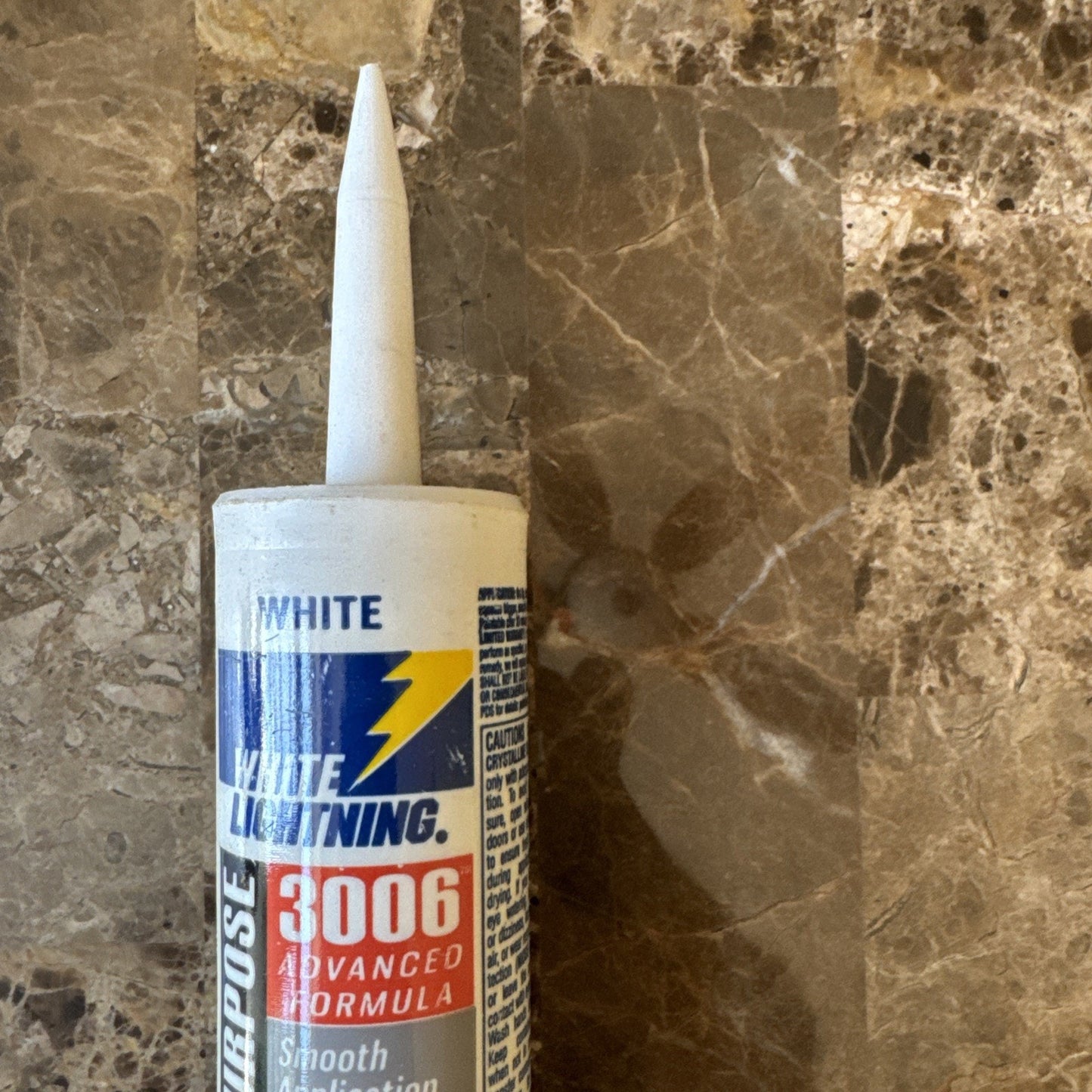 White Lightning 3006 Advanced Formula multi-purpose adhesive tube with a pointed nozzle, placed on a polished brown marble surface with a visible shadow.
