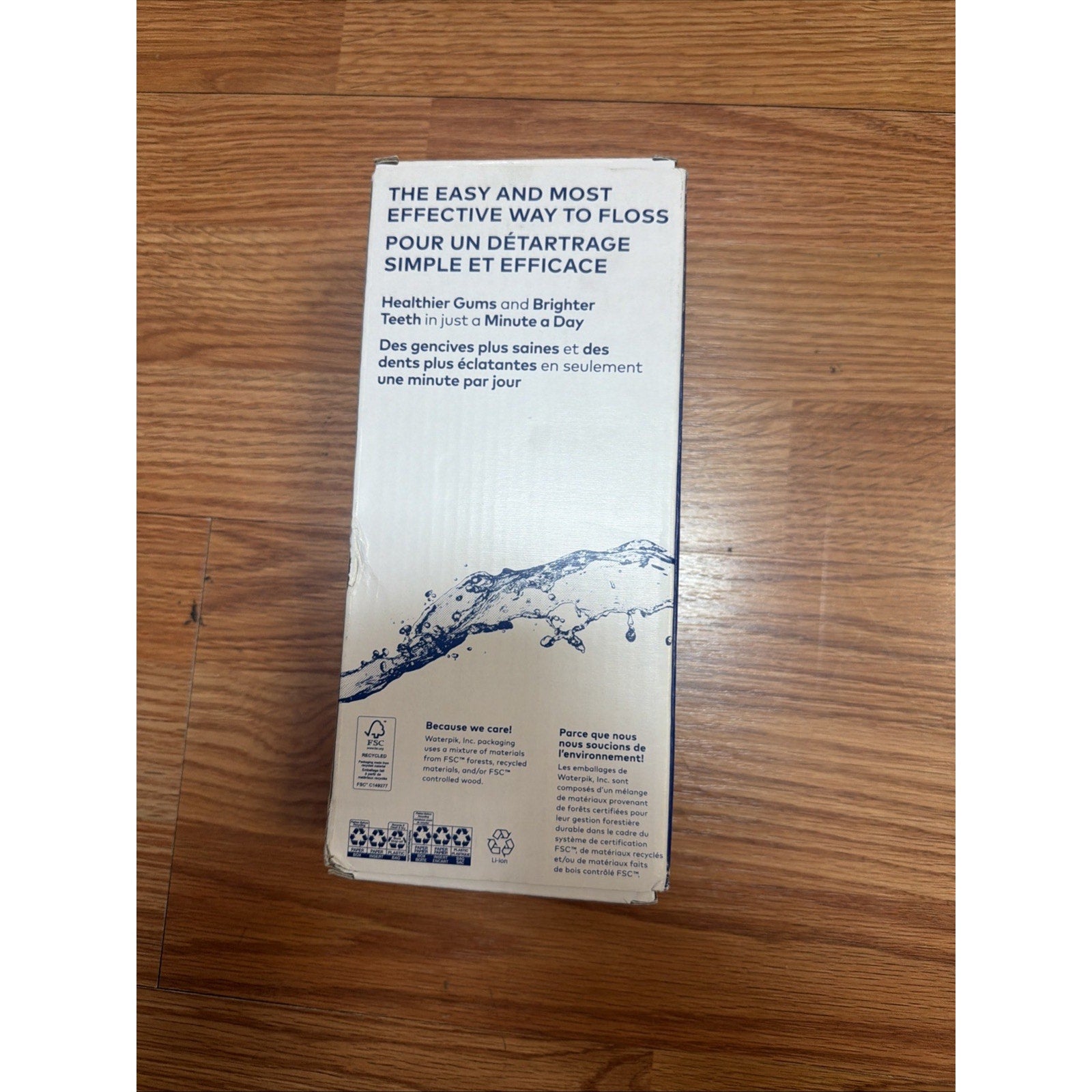 White cardboard product box with bilingual text promoting an effective flossing method for healthier gums and brighter teeth in just one minute, displayed on a wooden floor.