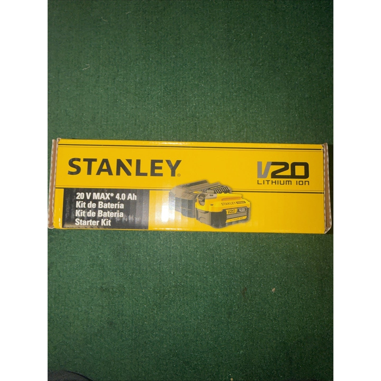 Yellow Stanley V20 Lithium Ion battery starter kit packaging box displaying 20V MAX 4.0 Ah capacity with bilingual labeling in English and Spanish on a green carpet background.