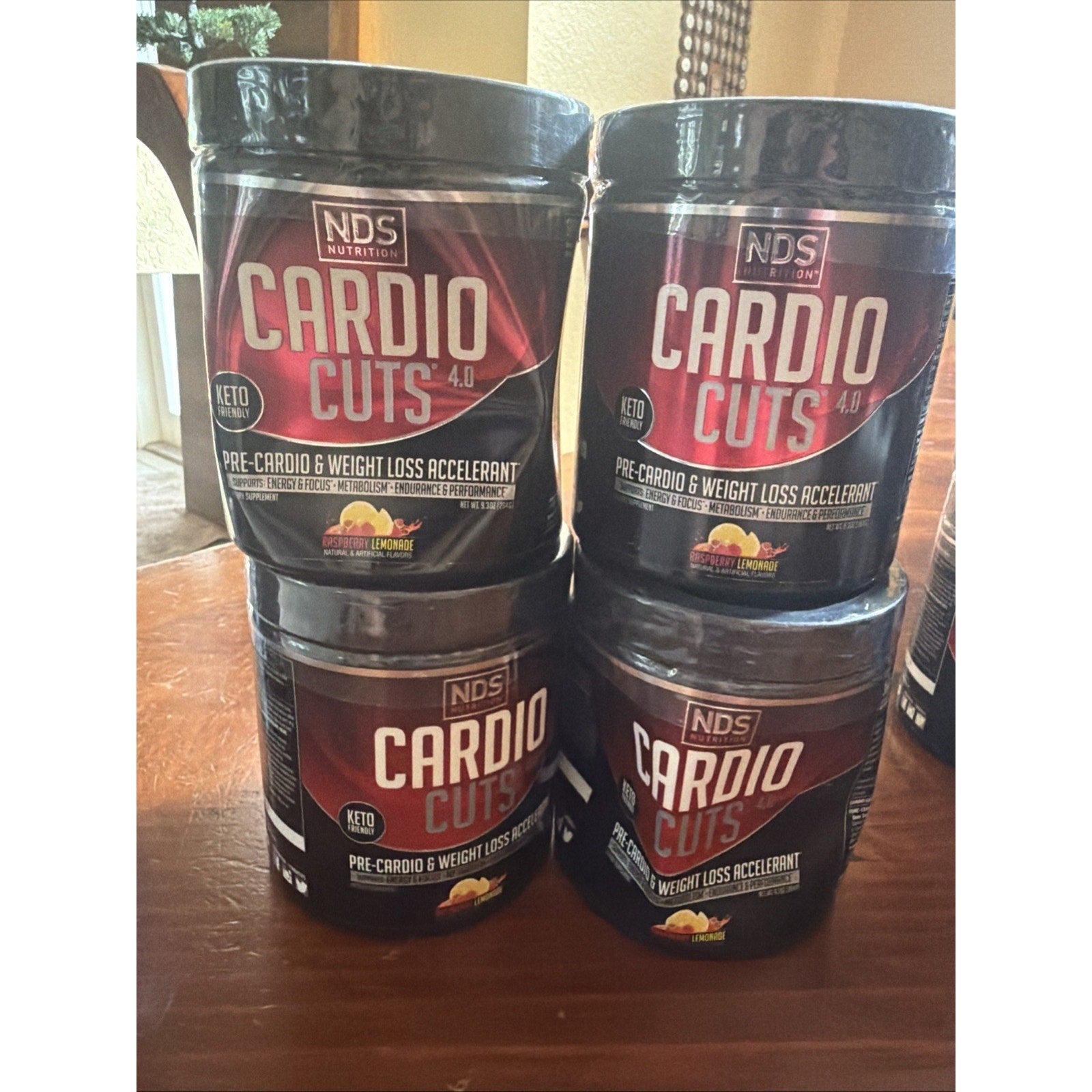 Four black containers of a pre-cardio and weight loss accelerator supplement stacked on a wooden surface with a lemon mango flavor label and keto-friendly badge.