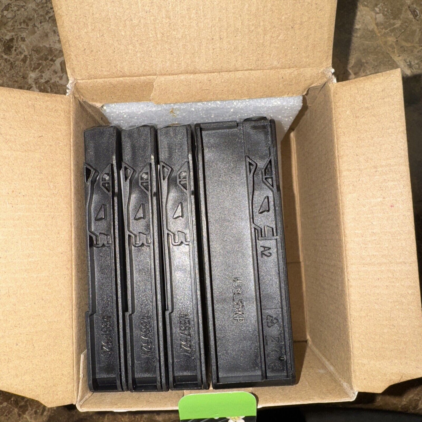 Pack of four black printer ink cartridges labeled 952 XL inside open brown cardboard box on marble surface