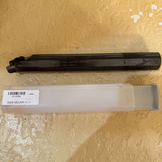 Dark metal cutting tool with multiple cutting edges on one end, engraved with specifications and resting above a translucent plastic case labeled with a product code, set on a textured yellow surface.