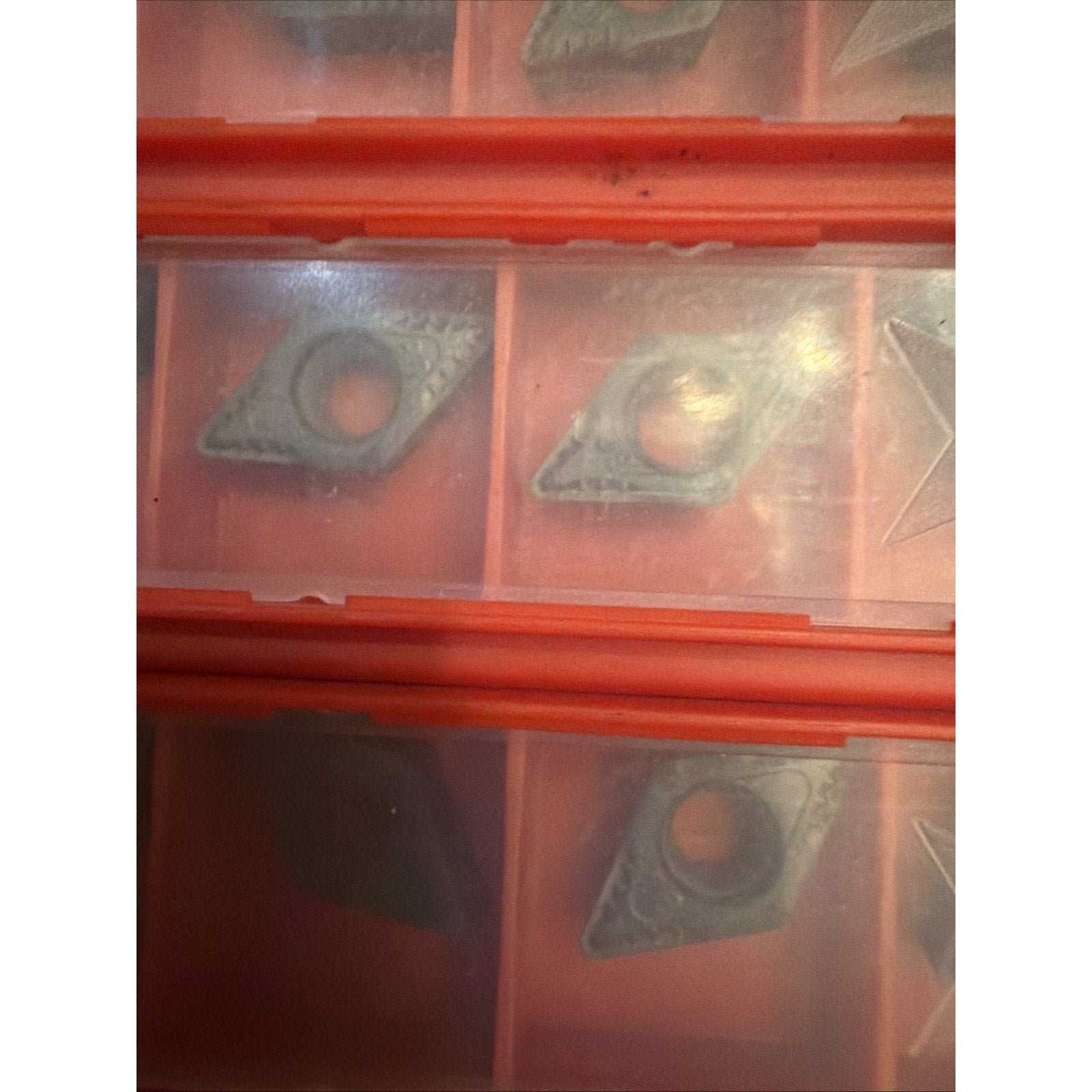 Red plastic organizer with multiple compartments containing small, triangular-shaped metal inserts, each with a circular hole near the center, visible through a translucent lid.