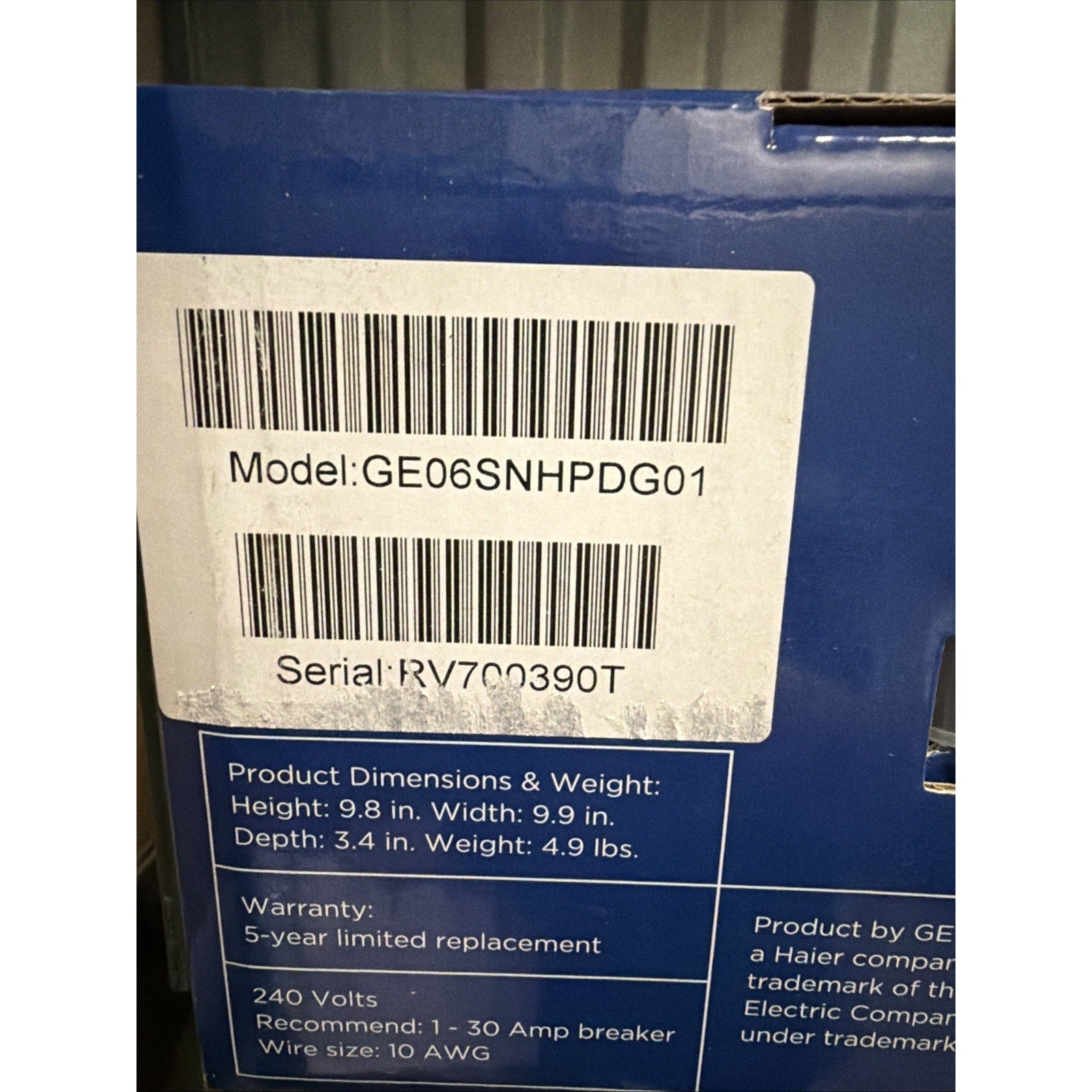 White label on a blue box showing model number GE06SNHPDG01, serial number RV700390T, product dimensions with height 9.8 in, width 9.9 in, depth 3.4 in, weight 4.9 lbs, and warranty details for 5-year limited replacement.