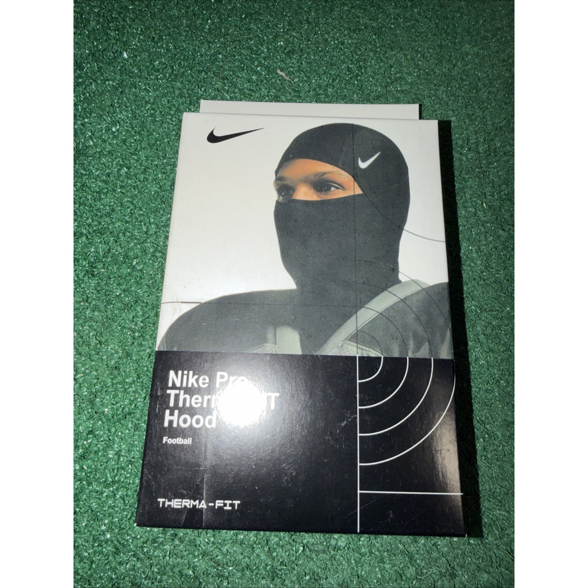 Box packaging for a Nike Pro Therma-FIT Hood designed for football, featuring an image of a person wearing the black hood with the Nike swoosh visible on the forehead area.