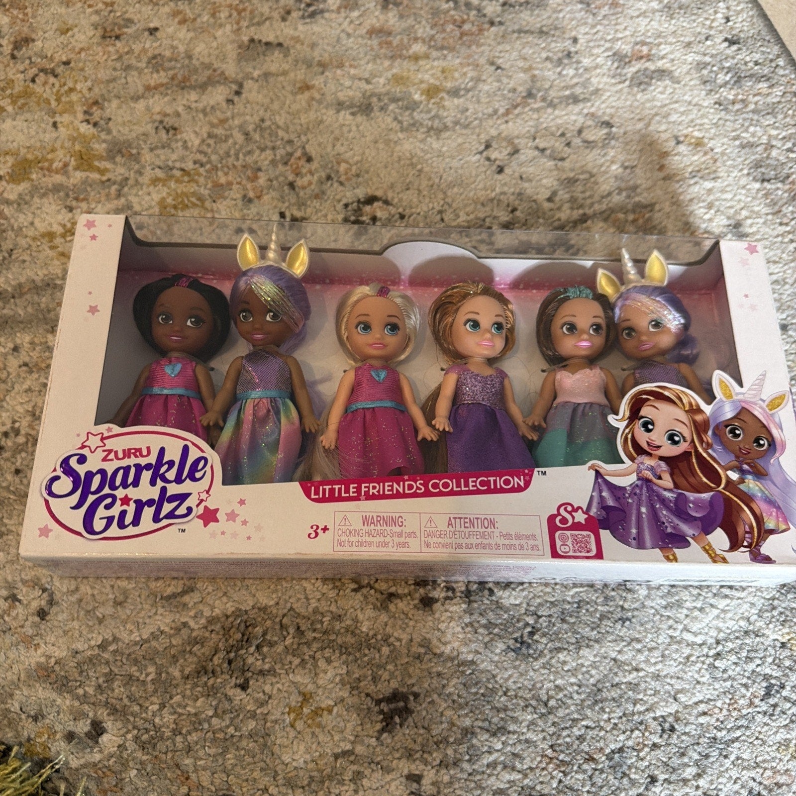 Set of six small dolls with diverse skin tones and colorful outfits, some with glittery purple dresses and golden animal ear headbands, packaged in a white box labeled "Sparkle Girlz Little Friends Collection.