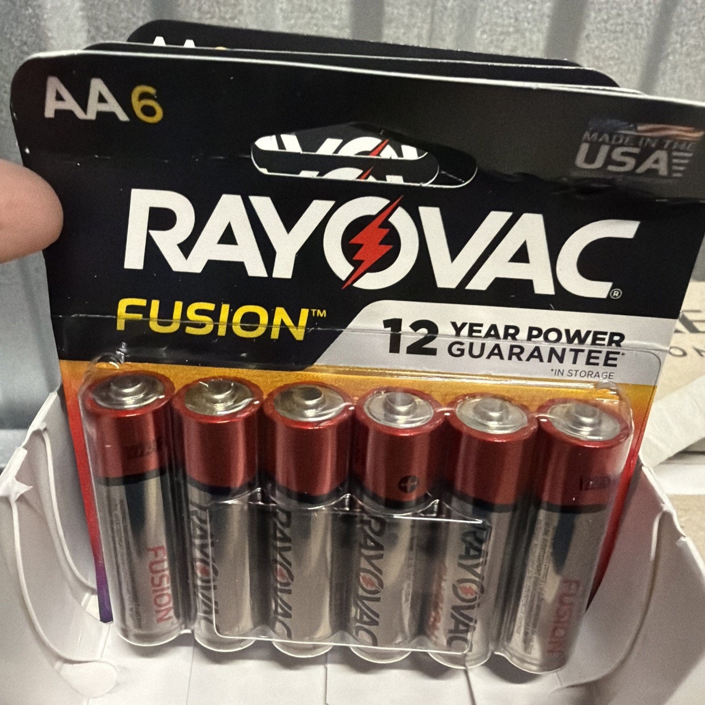 Pack of six AA Rayovac Fusion batteries with silver and red casing, featuring 12-year power guarantee and made in the USA, displayed in black and orange retail packaging.