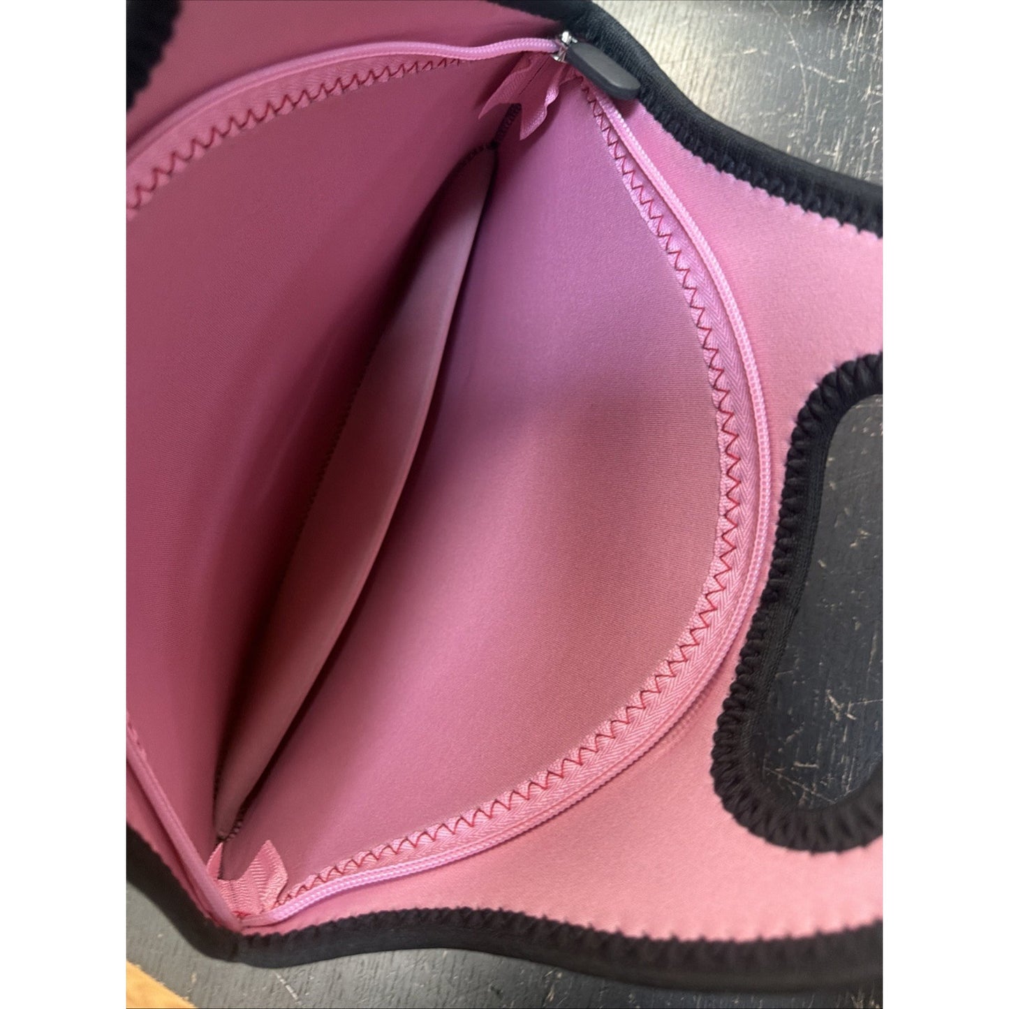 Interior view of a soft pink neoprene lunch tote showing the smooth lining, reinforced zigzag stitching along the edges, and a curved zipper opening with black trim detailing.
