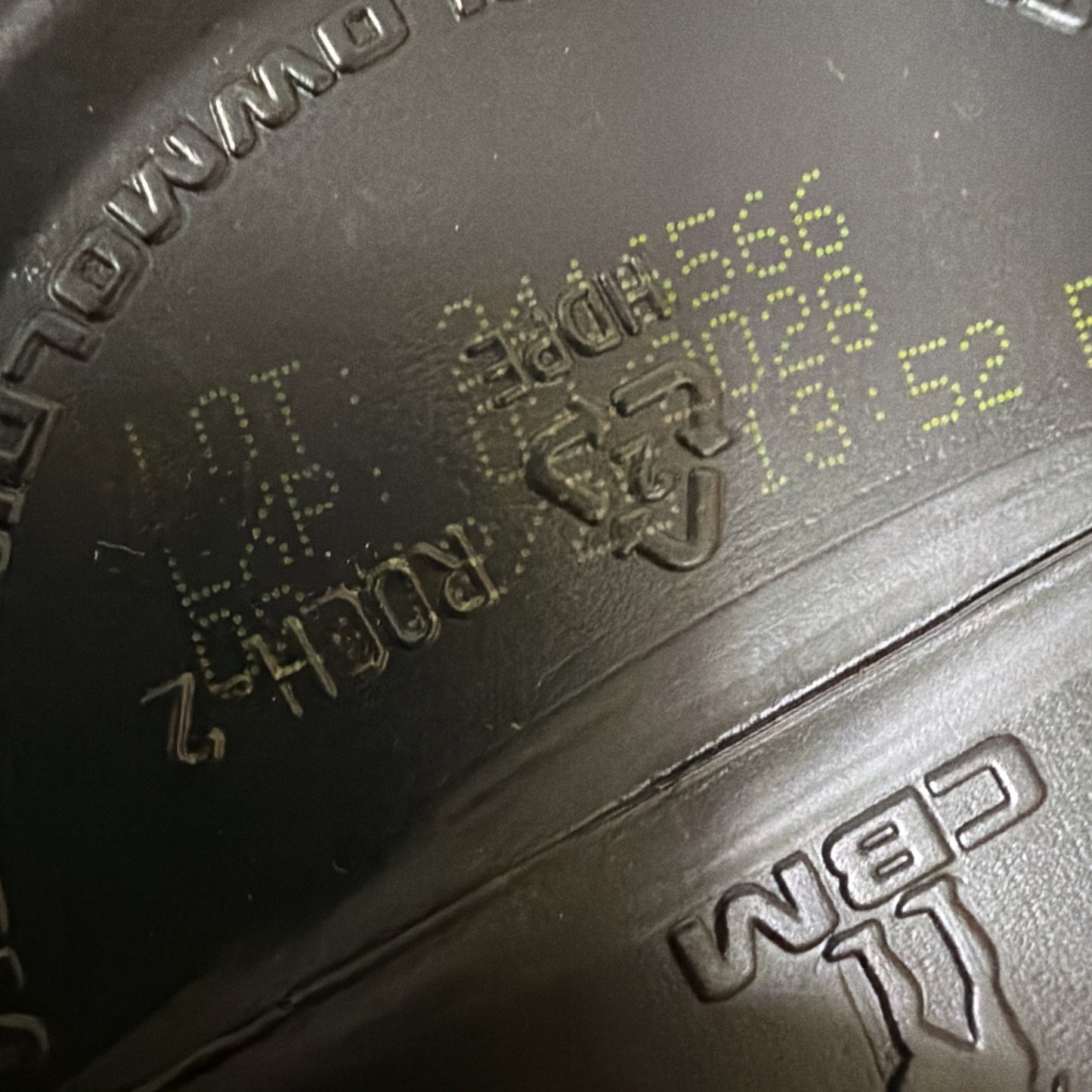 Close-up of a dark brown plastic surface featuring a faint yellow printed batch code, recycling symbol with number 2 inside, and raised molded text including "CBM.