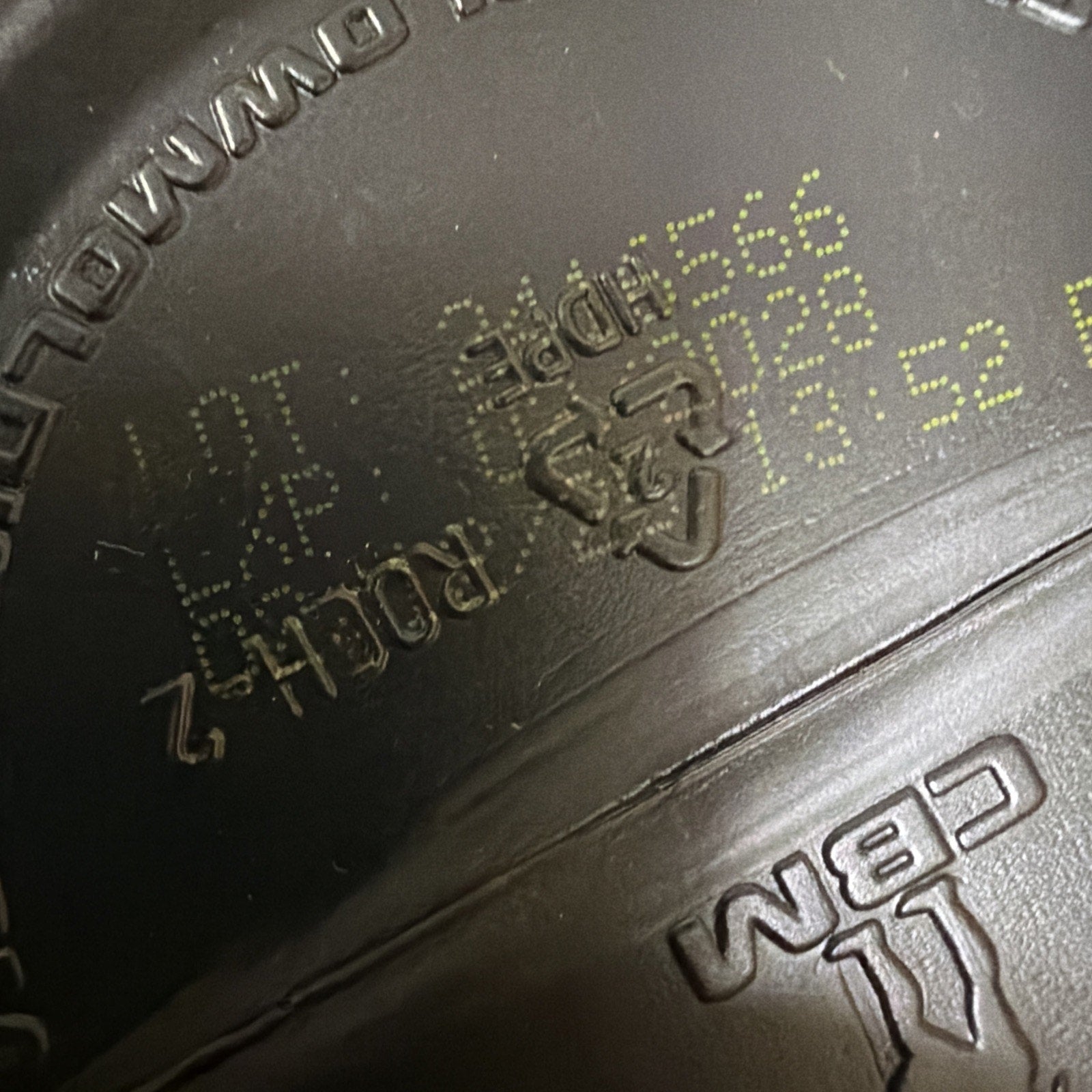 Close-up of a dark brown plastic surface featuring a faint yellow printed batch code, recycling symbol with number 2 inside, and raised molded text including "CBM.