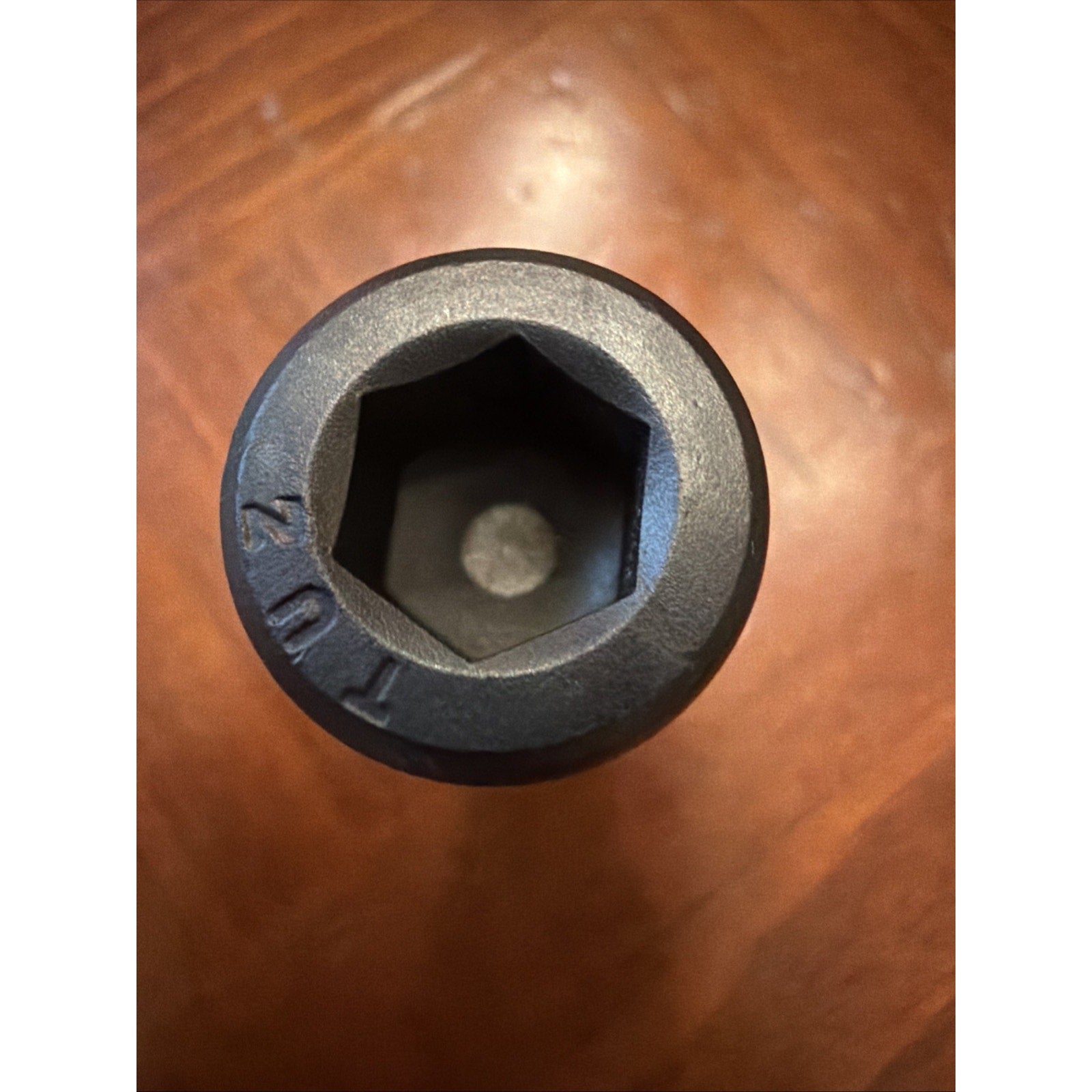 Close-up of the top of a black hexagonal socket tool with the marking "T024" visible on its outer edge, placed on a wood surface with a warm tone.
