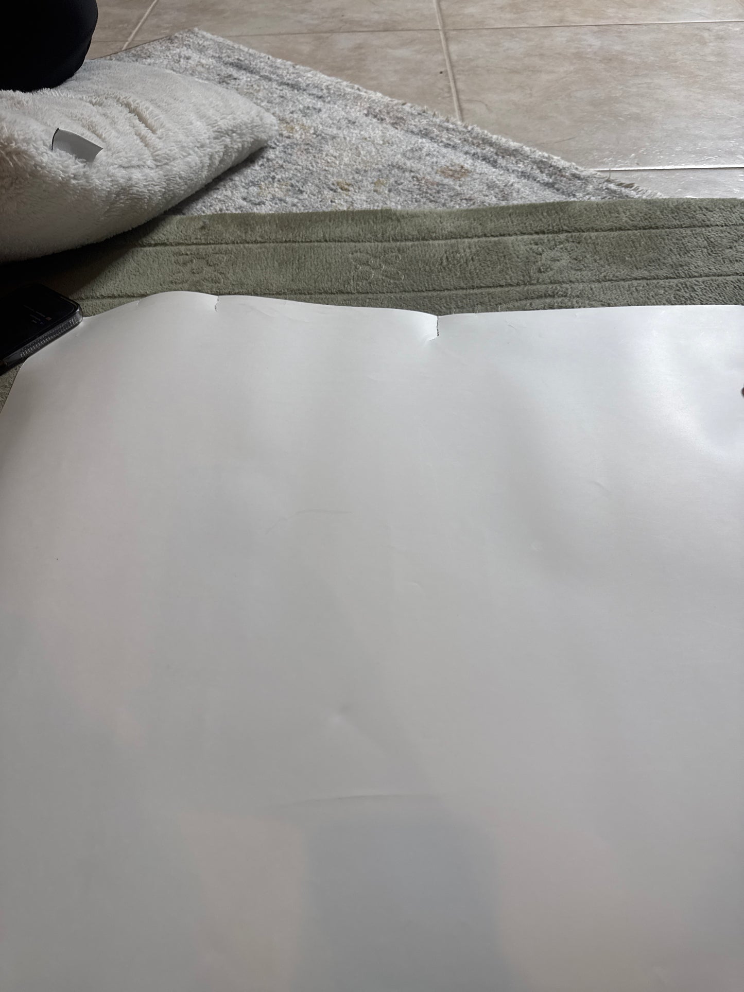 Blank white poster or photo laid on carpet and tiled floor, partially folded at the top edge