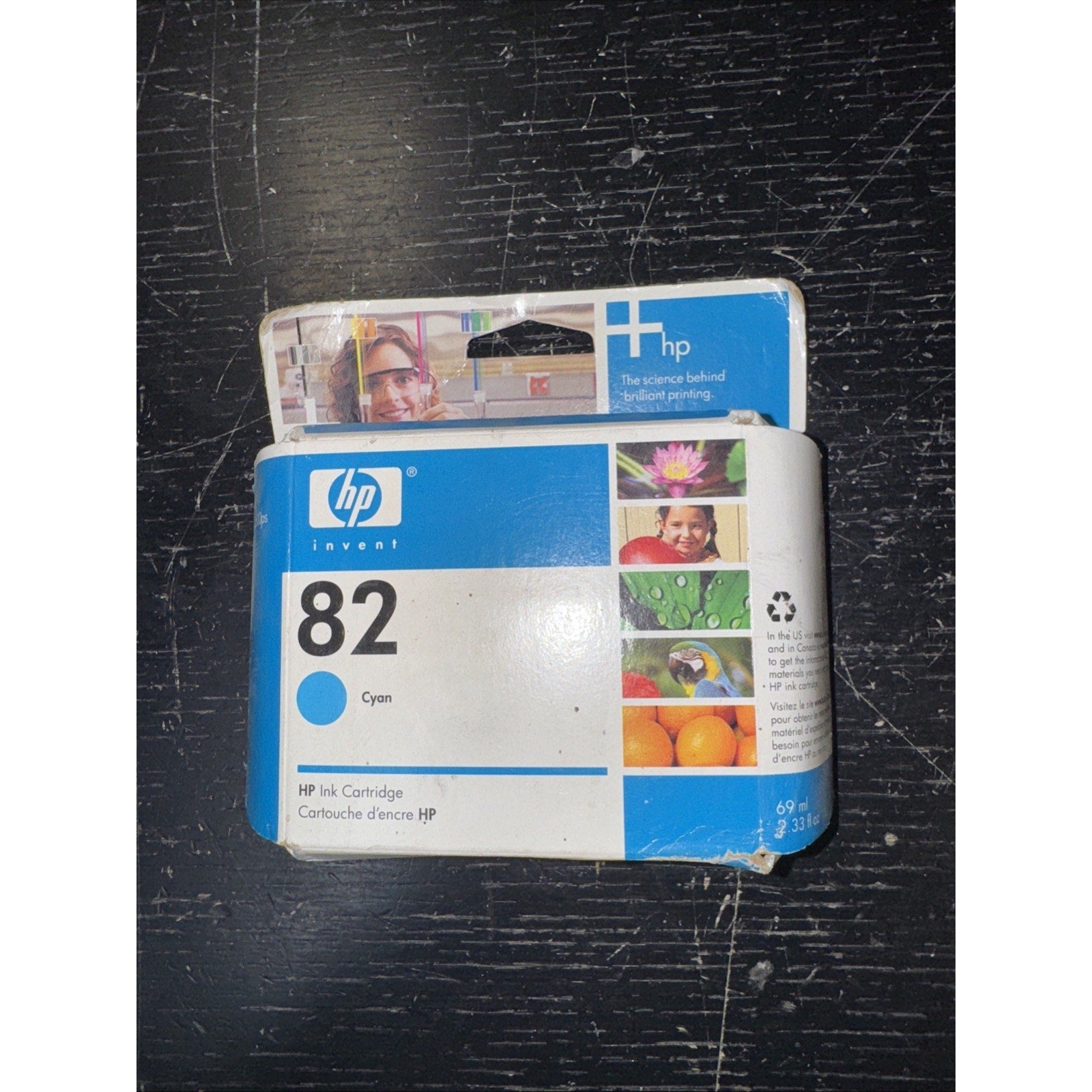 Genuine HP 82 cyan ink cartridge box with product images and HP logo on worn packaging on black surface