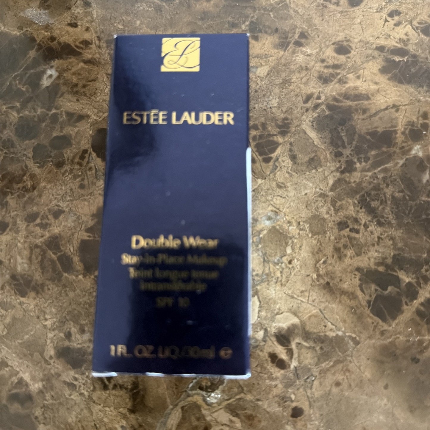 Dark blue rectangular box of Estée Lauder Double Wear Stay-in-Place Makeup foundation with gold lettering and logo on a brown marbled surface.