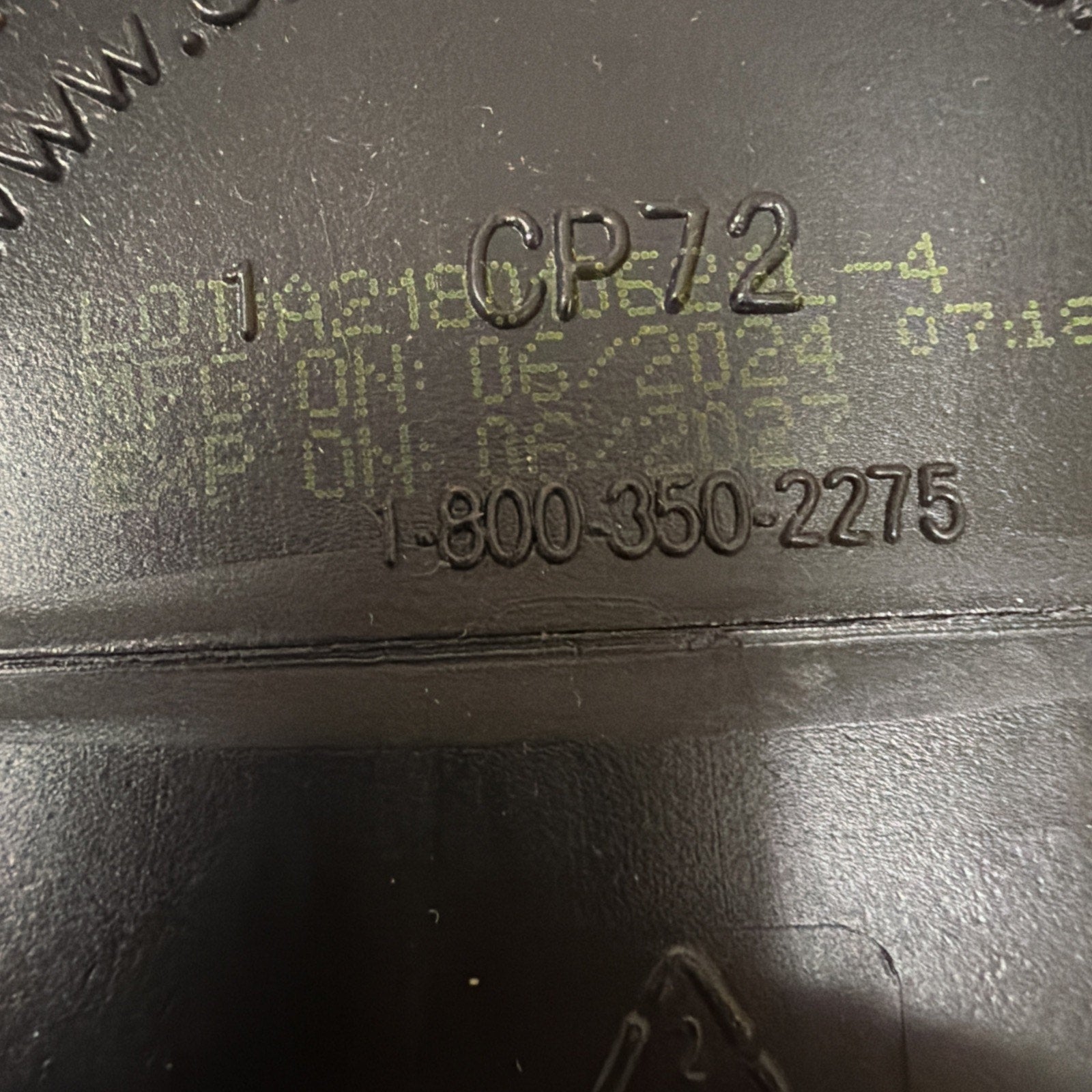 Close-up of manufacturing details embossed and printed on a black plastic surface, showing the code CP72-4, a customer service phone number, and faint yellow print with production and expiration dates.