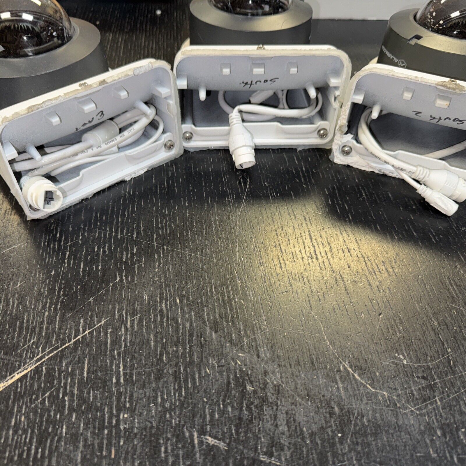 Lot of 3 Alarm.com surveillance dome cameras with infrared and attached cables shown from base side on black surface