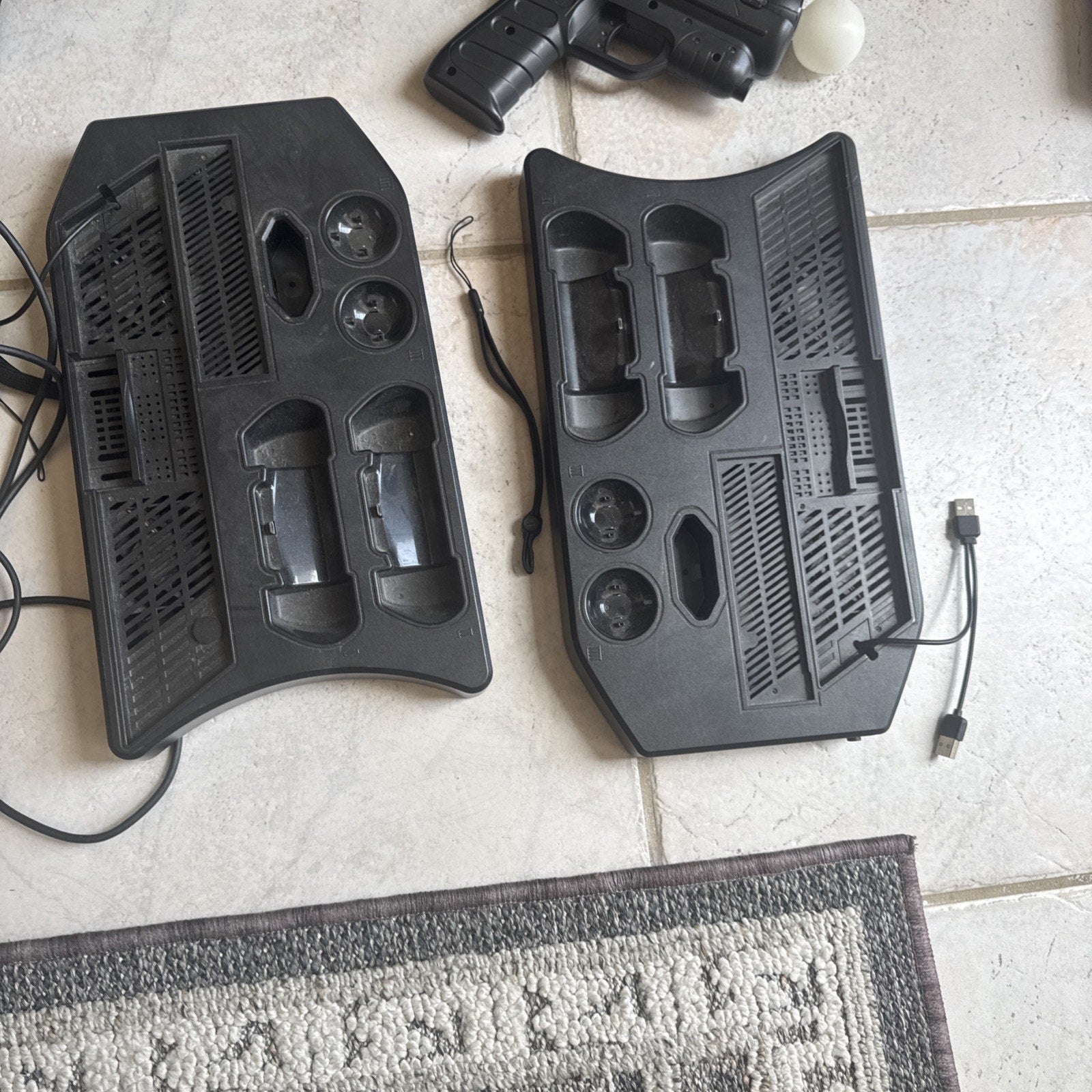 Two black charging stations for PlayStation VR controllers with USB cables and a VR gun accessory on tiled floor