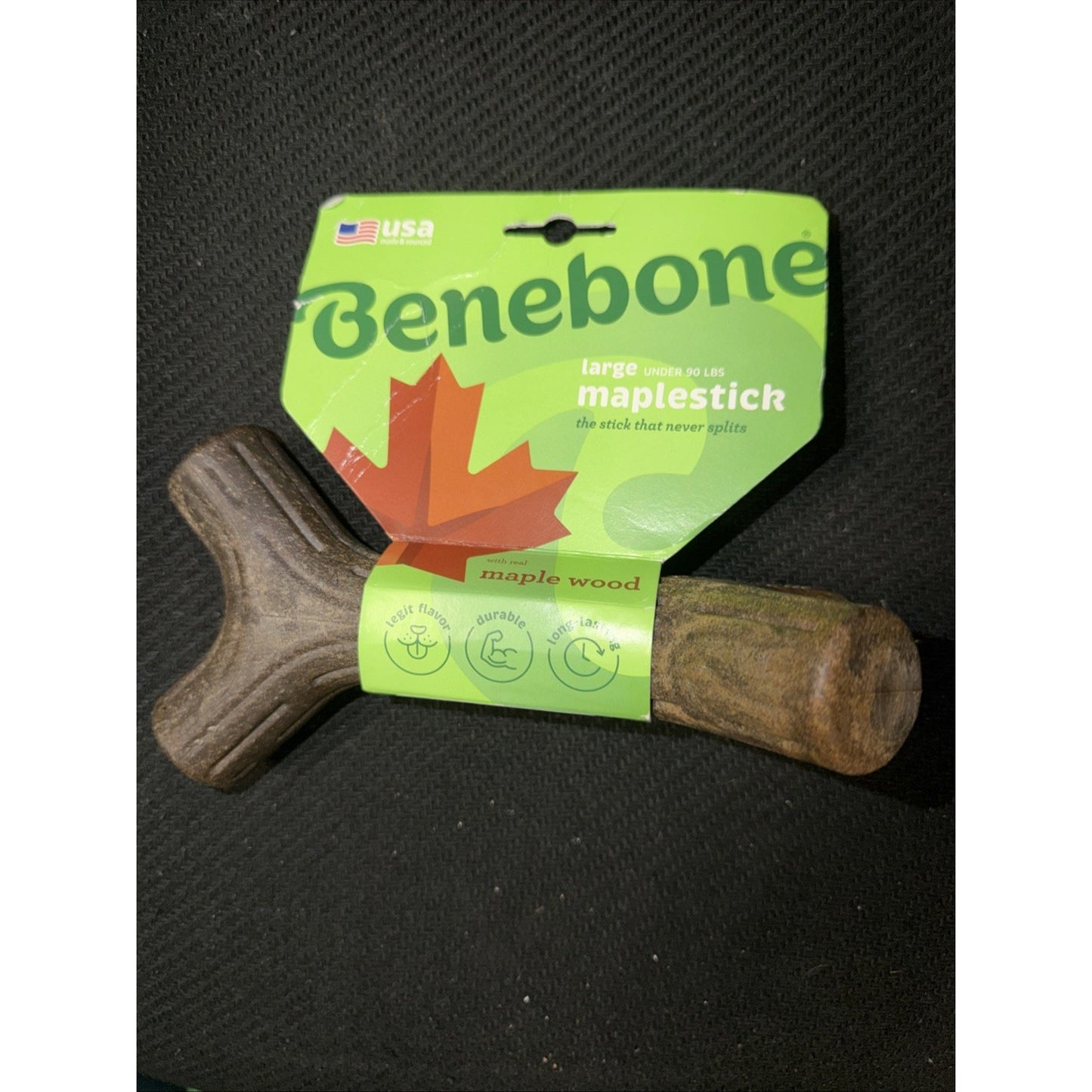 Natural maple wood dog chew in the shape of a large stick with green and orange Benebone packaging featuring a maple leaf design and product details on a black background.