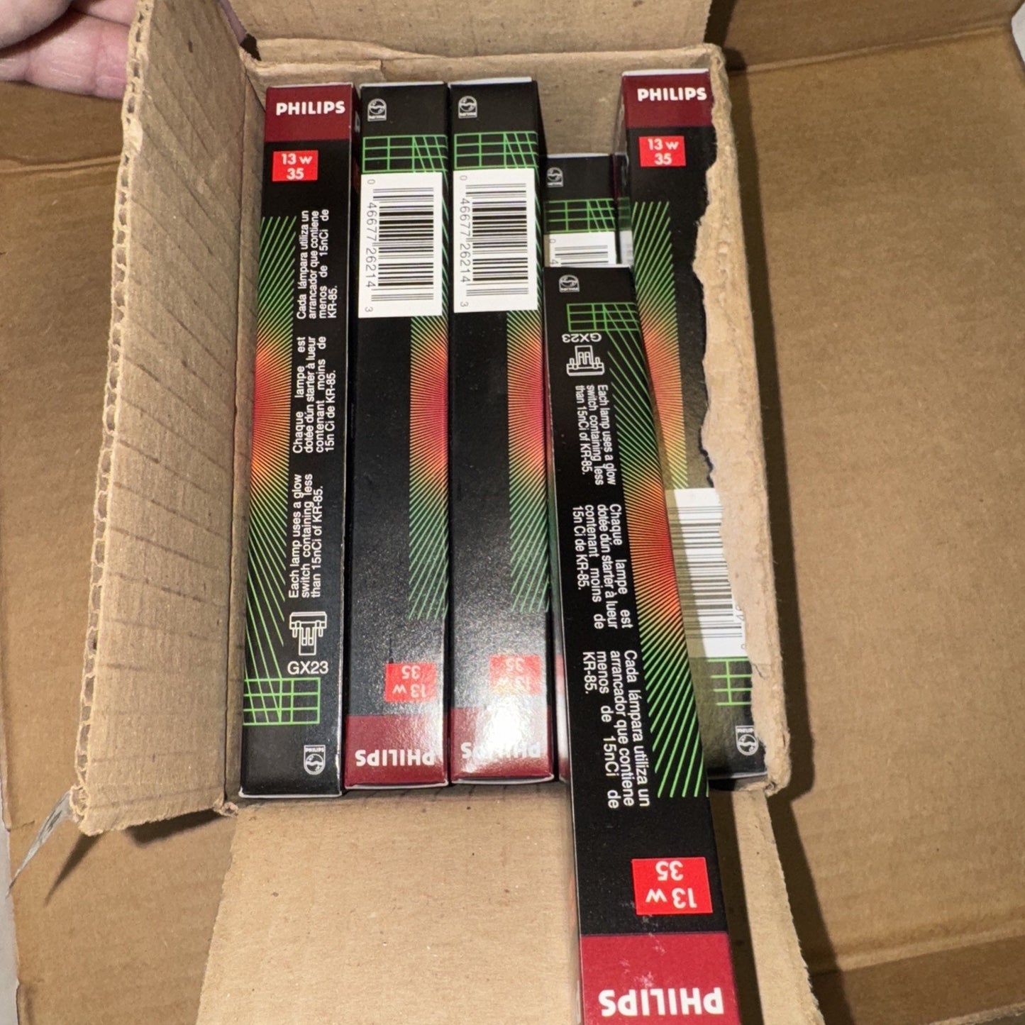 Open cardboard box containing multiple Philips PL-S 13W/35 fluorescent lamp light bulb packages with black and red design