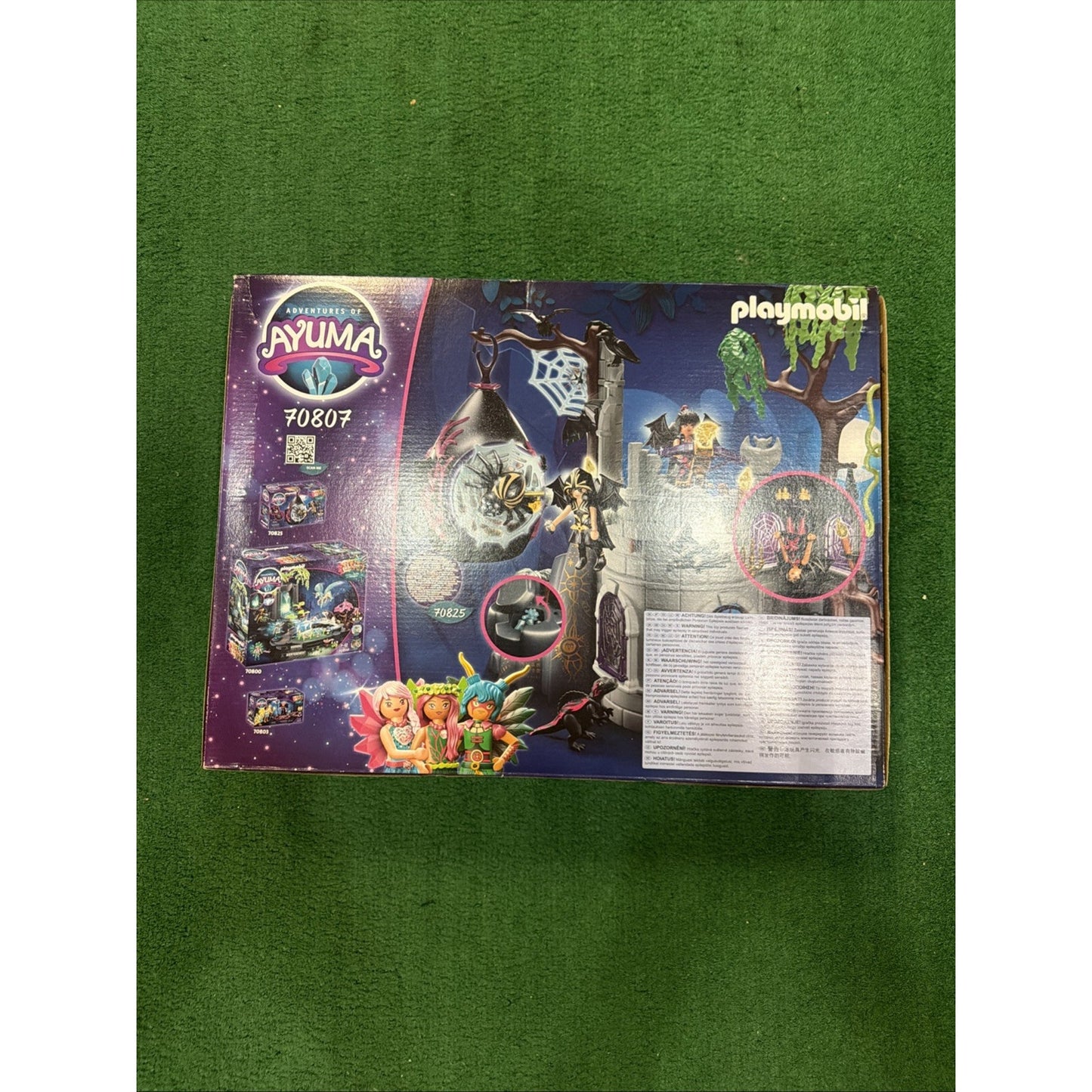 Playmobil Ayuma playset box featuring a dark tower with spider web, multiple fairy figurines, colorful magical creatures, and accessories shown on a green textured surface.