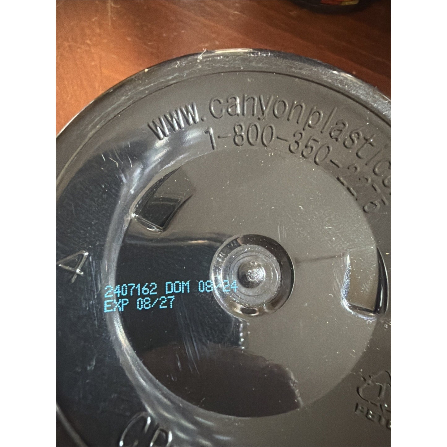Black plastic container lid with molded recycling symbols, website URL, customer service phone number, and printed manufacturing and expiration dates.