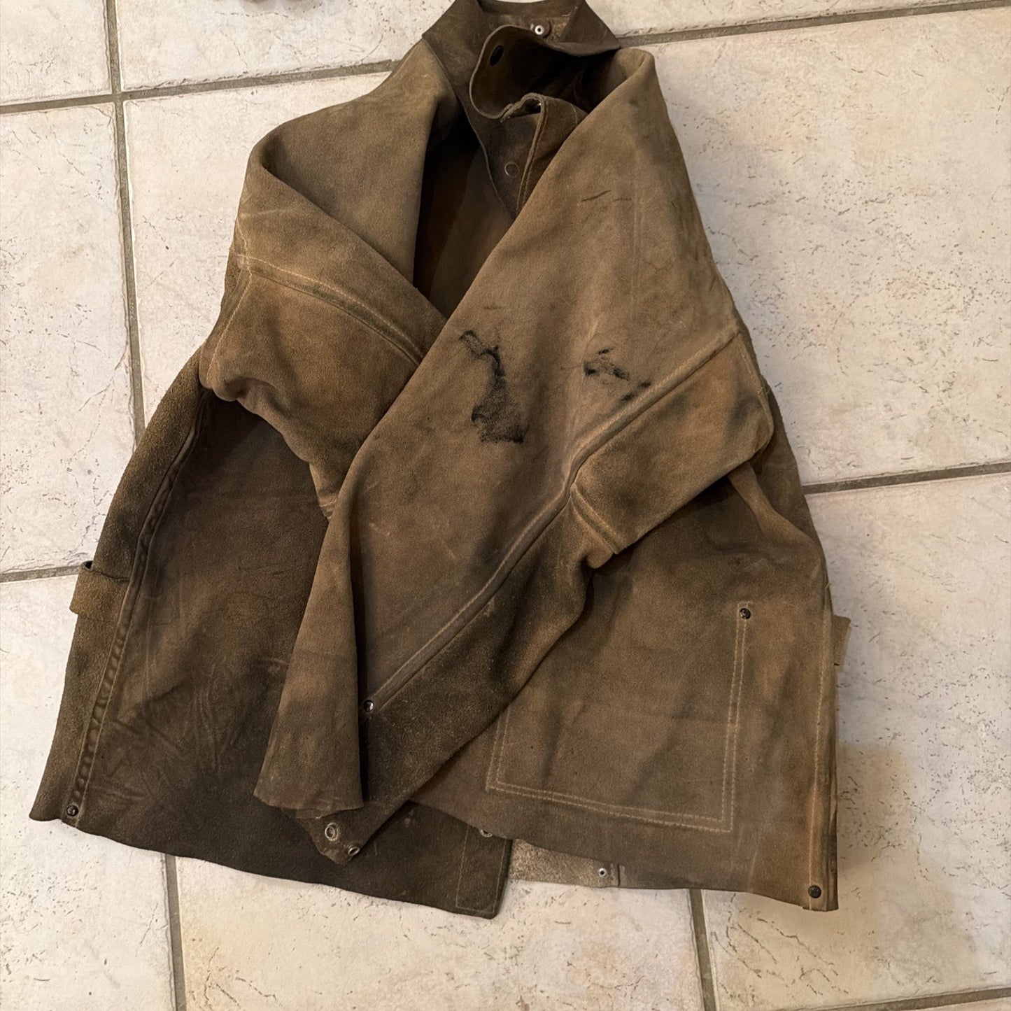 Heavy-duty leather welding jacket coat in brown with visible wear and protective stitching on tiled floor