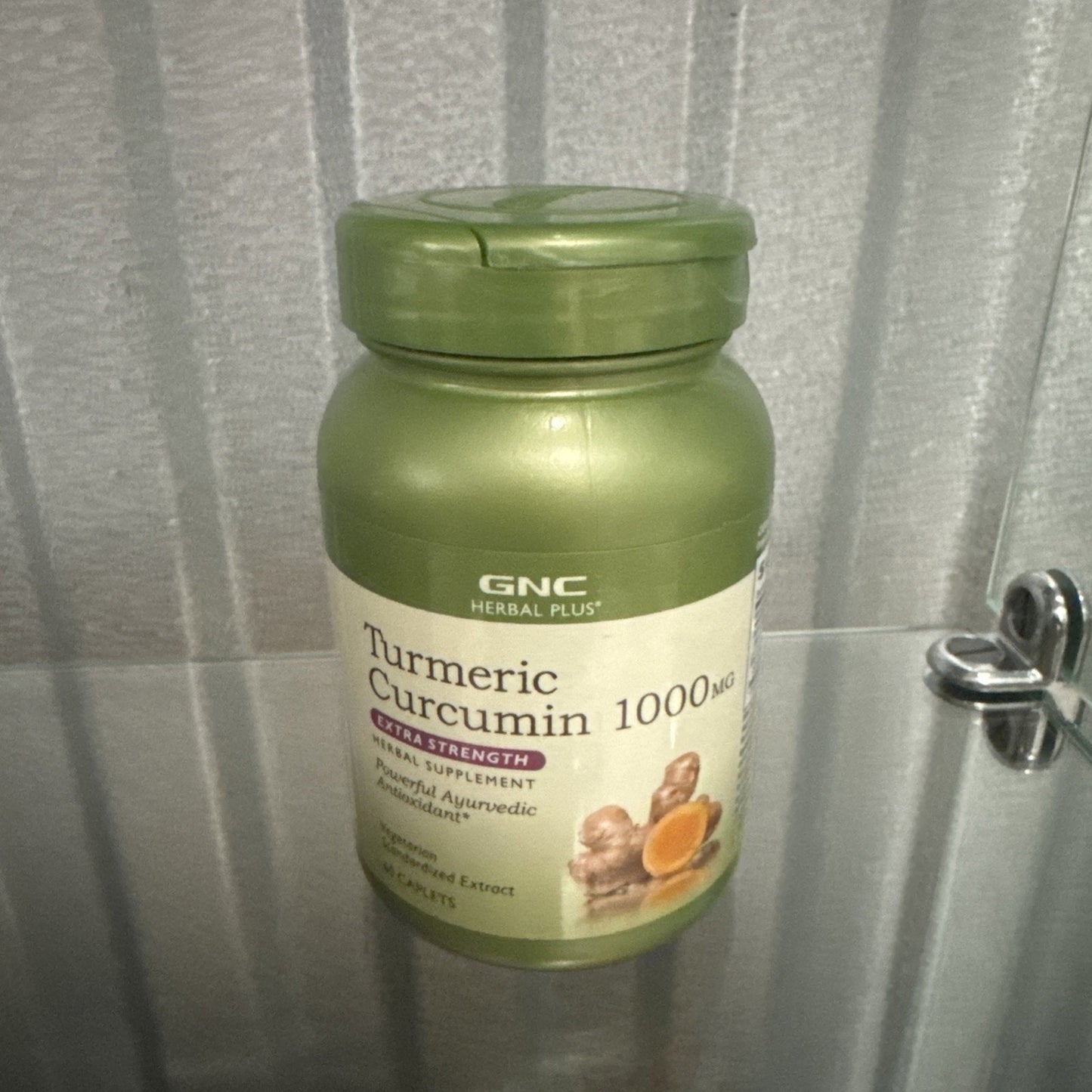 Green plastic bottle of GNC Herbal Plus Turmeric Curcumin 1000 mg dietary supplement with a beige label featuring turmeric root images and dosage information.