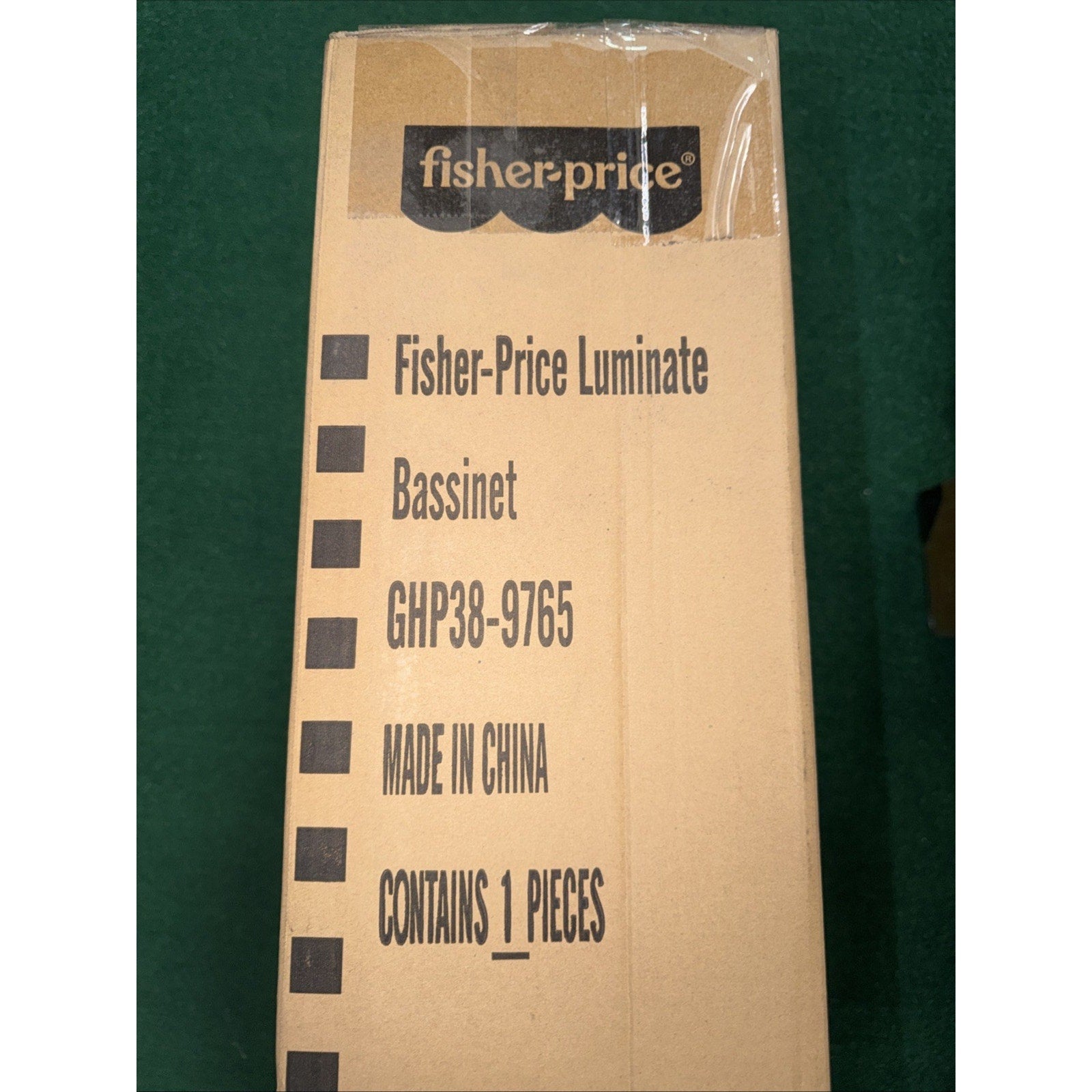 Brown cardboard shipping box with Fisher-Price branding, listing product details including model number, origin as made in China, and contents information on a green surface.