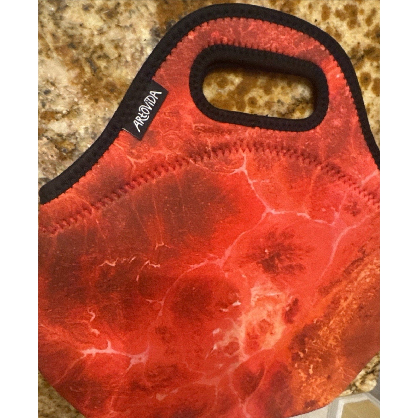 Red Artovida neoprene lunch bag with black trim and top handle stitched on marbled countertop surface