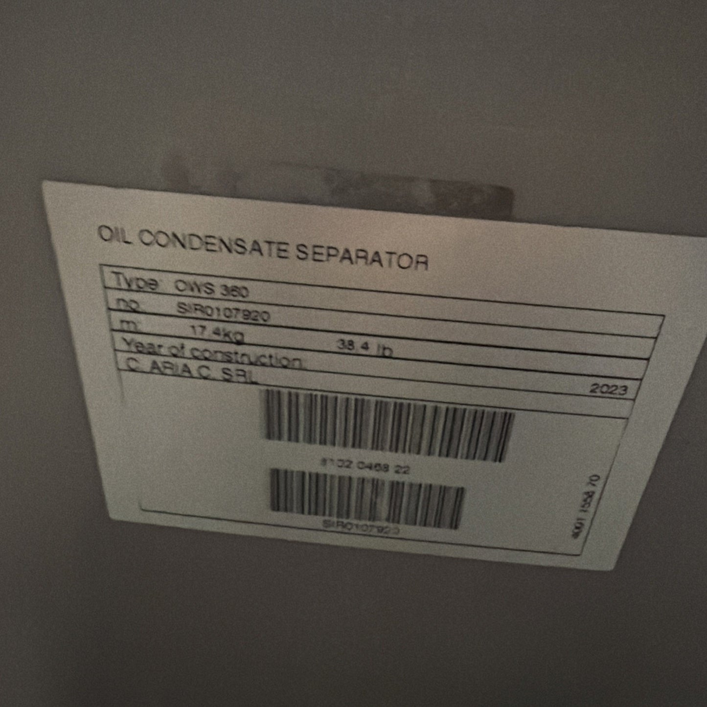 White label attached to a gray surface, showing printed details including "OIL CONDENSATE SEPARATOR," type information, serial number, weight in kilograms and pounds, construction year 2023, and two barcodes.
