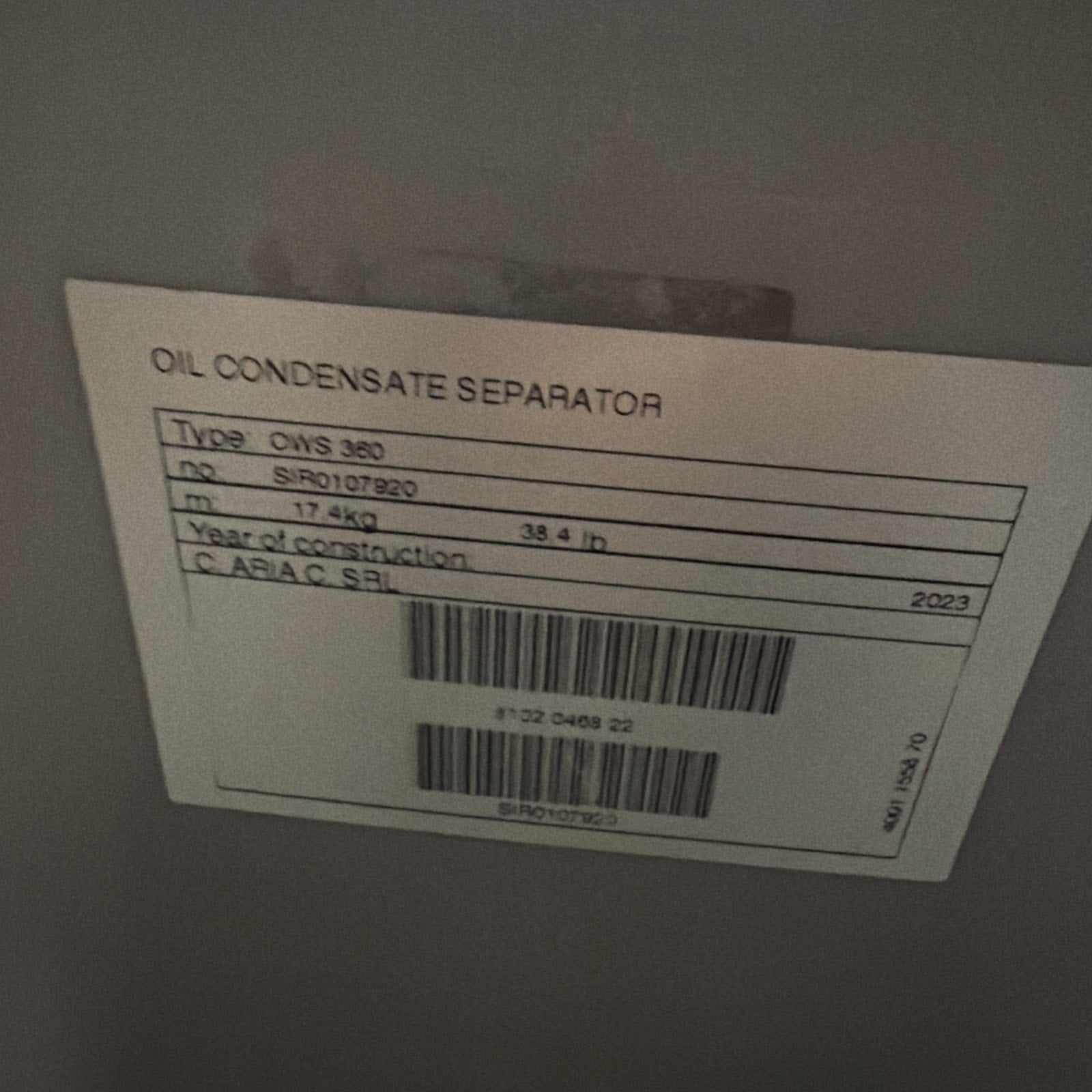 White label attached to a gray surface, showing printed details including "OIL CONDENSATE SEPARATOR," type information, serial number, weight in kilograms and pounds, construction year 2023, and two barcodes.