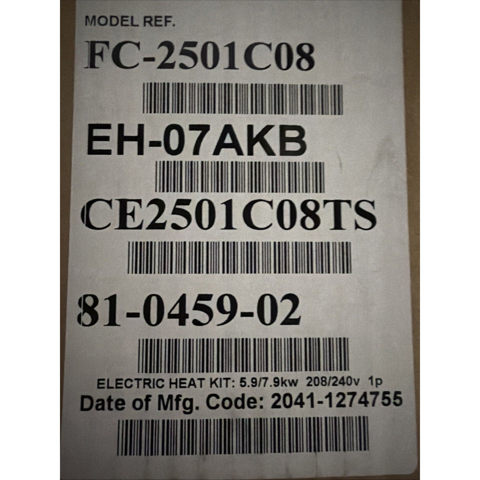 Close-up of a white label on cardboard displaying model and serial numbers, barcodes, and specifications for an electric heat kit with power ratings and manufacturing code.