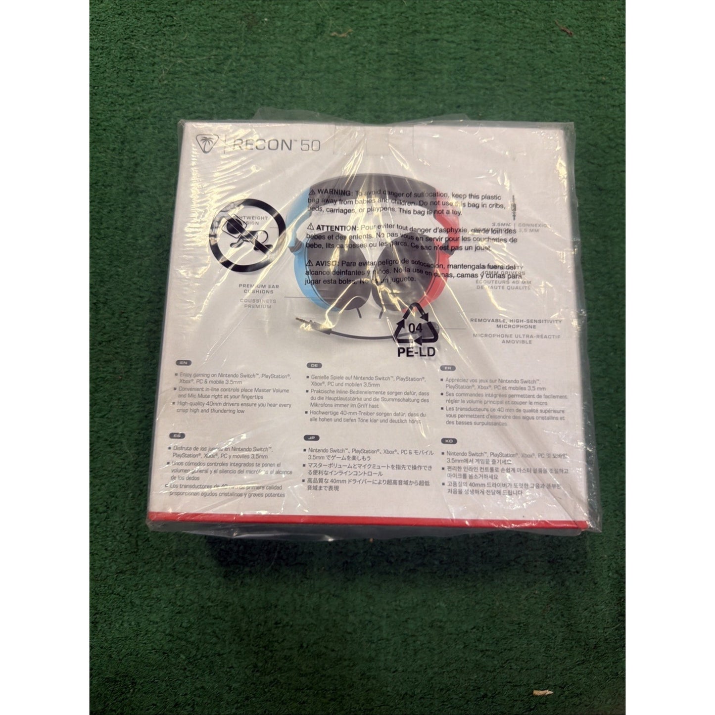 White product box for a Recon 50 gaming headset featuring blue and red ear cup illustrations, multilingual safety warnings, and a plastic wrap with a recycling symbol.