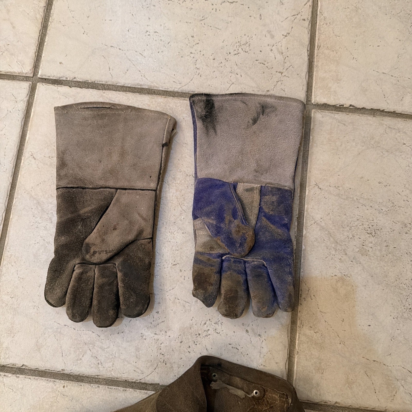Pair of well-worn heavy-duty leather welding gloves with extended cuffs on tiled floor background