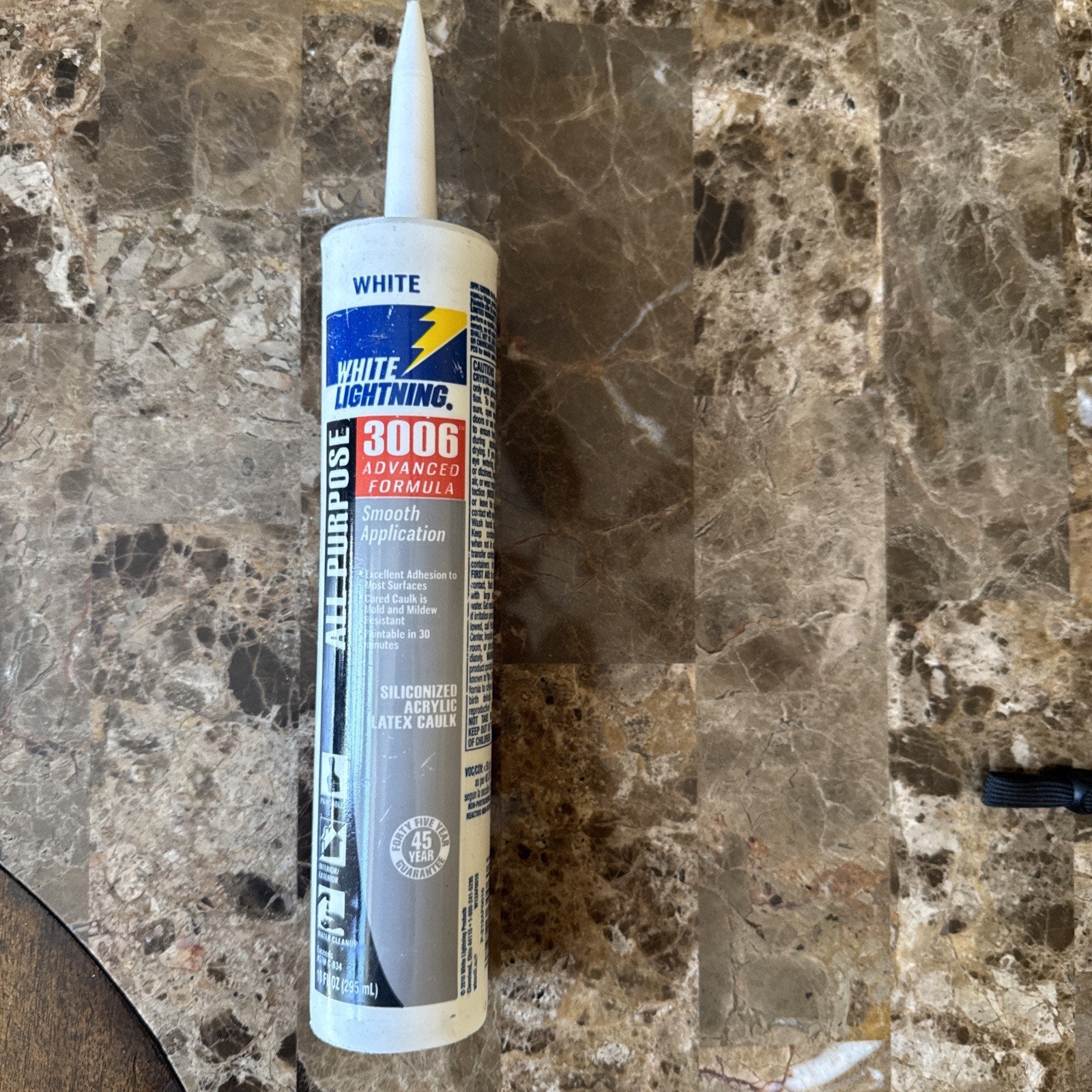 White Lightning 3006 all-purpose caulk tube with advanced formula for smooth application, featuring weather-resistant and paintable properties, standing upright on a marble surface.