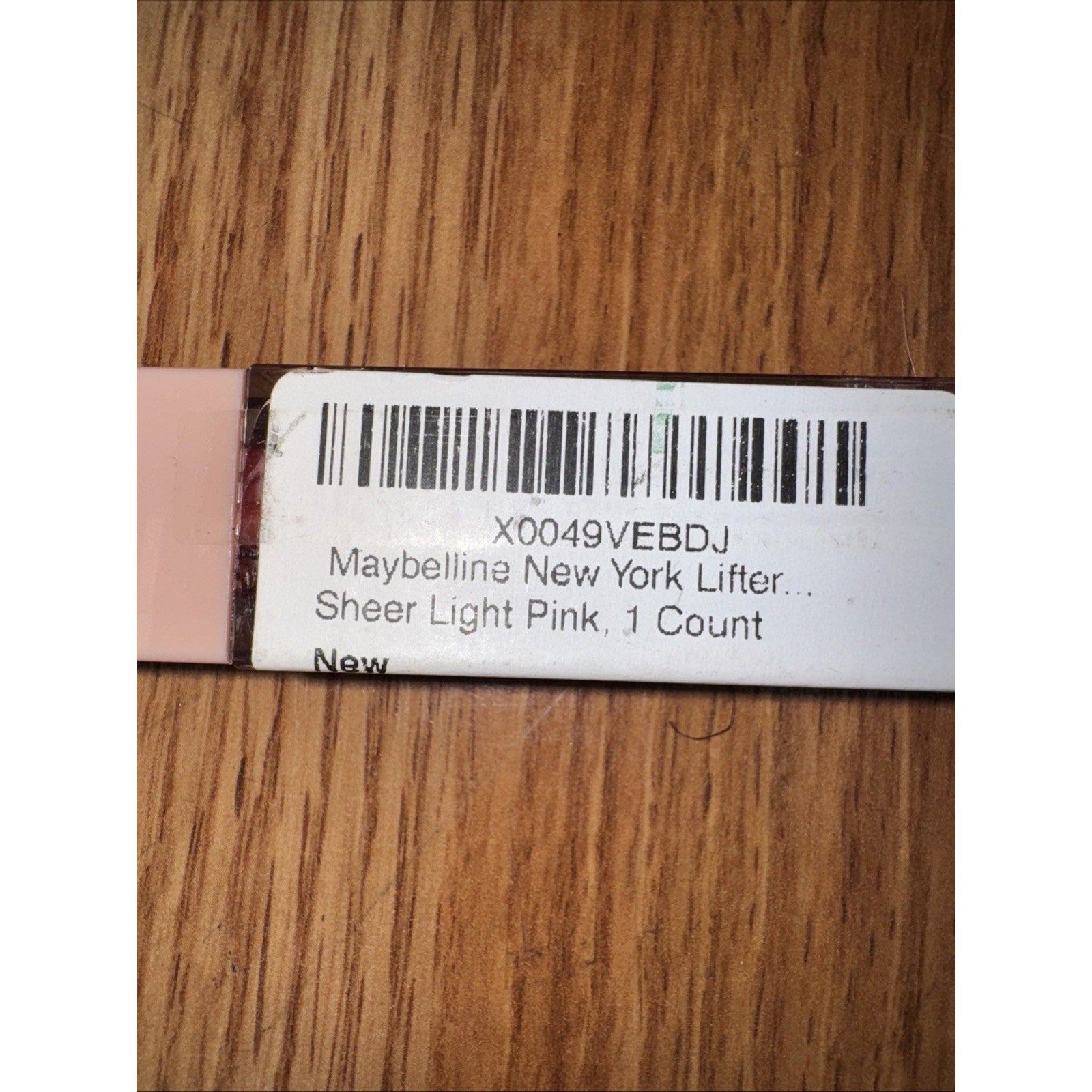 Barcode label for Maybelline New York Lifter Lip Gloss Sheer Light Pink 1 count on wooden surface