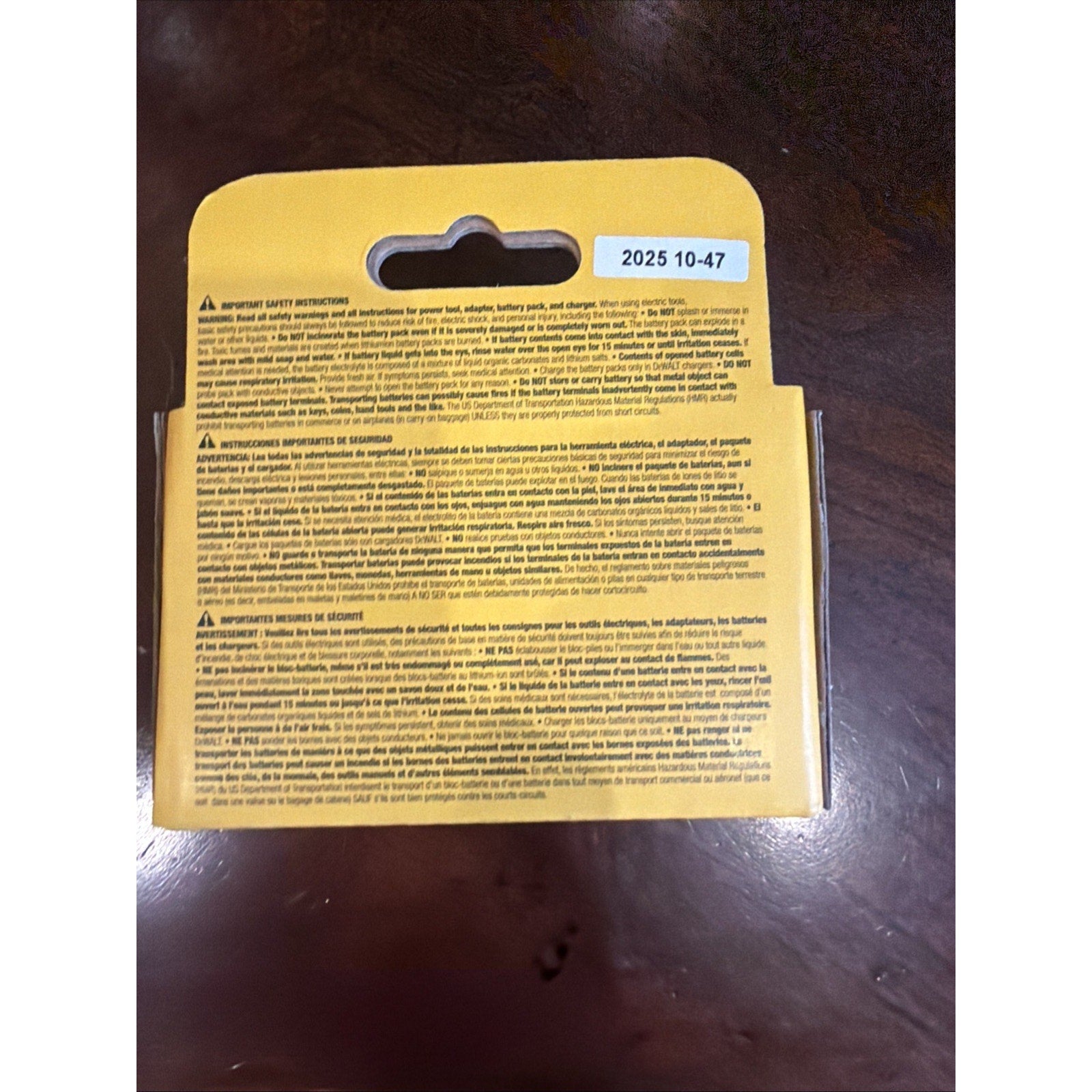 Yellow product packaging card showing safety instructions, warnings, and storage guidelines in multiple languages printed in black text on a dark wooden surface.