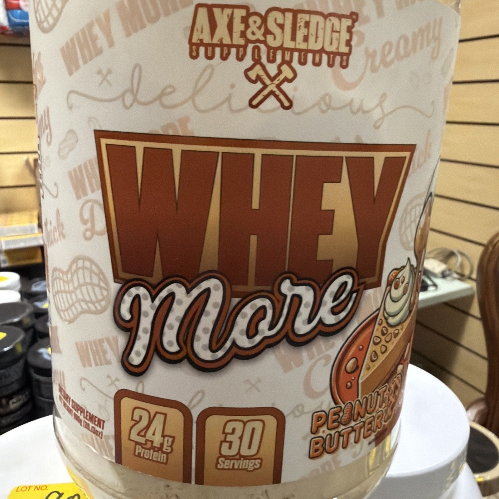 Container of Axe & Sledge Whey More protein powder in peanut butter flavor, featuring 24 grams of protein and 30 servings per container with beige and brown packaging.