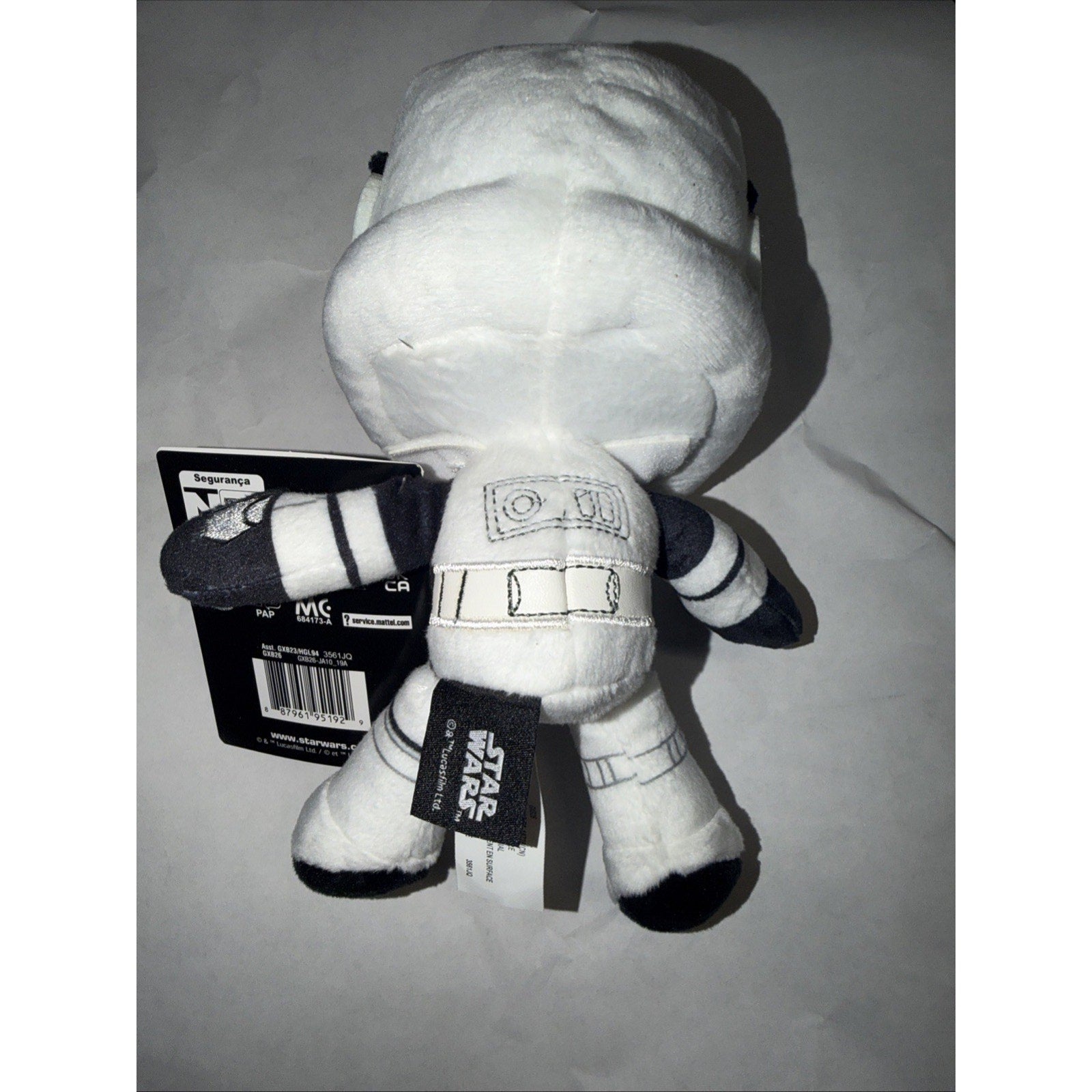 Small plush toy resembling a white Star Wars stormtrooper character with black and gray details, shown from the back with attached tags against a plain background.