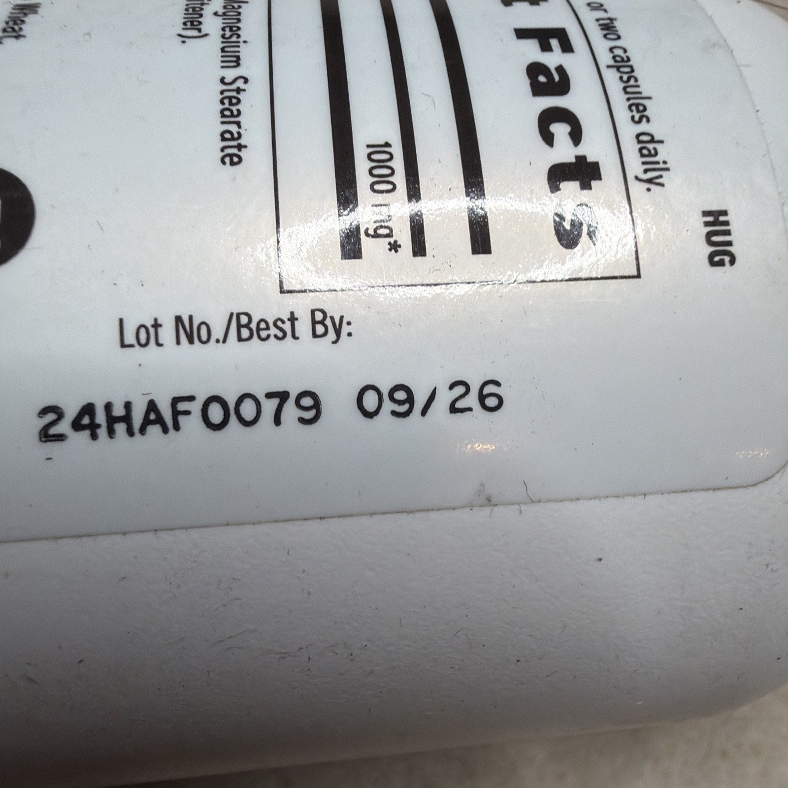 Close-up of a white supplement bottle label showing a lot number and expiration date printed in black ink, with partial nutritional facts and ingredient information visible.