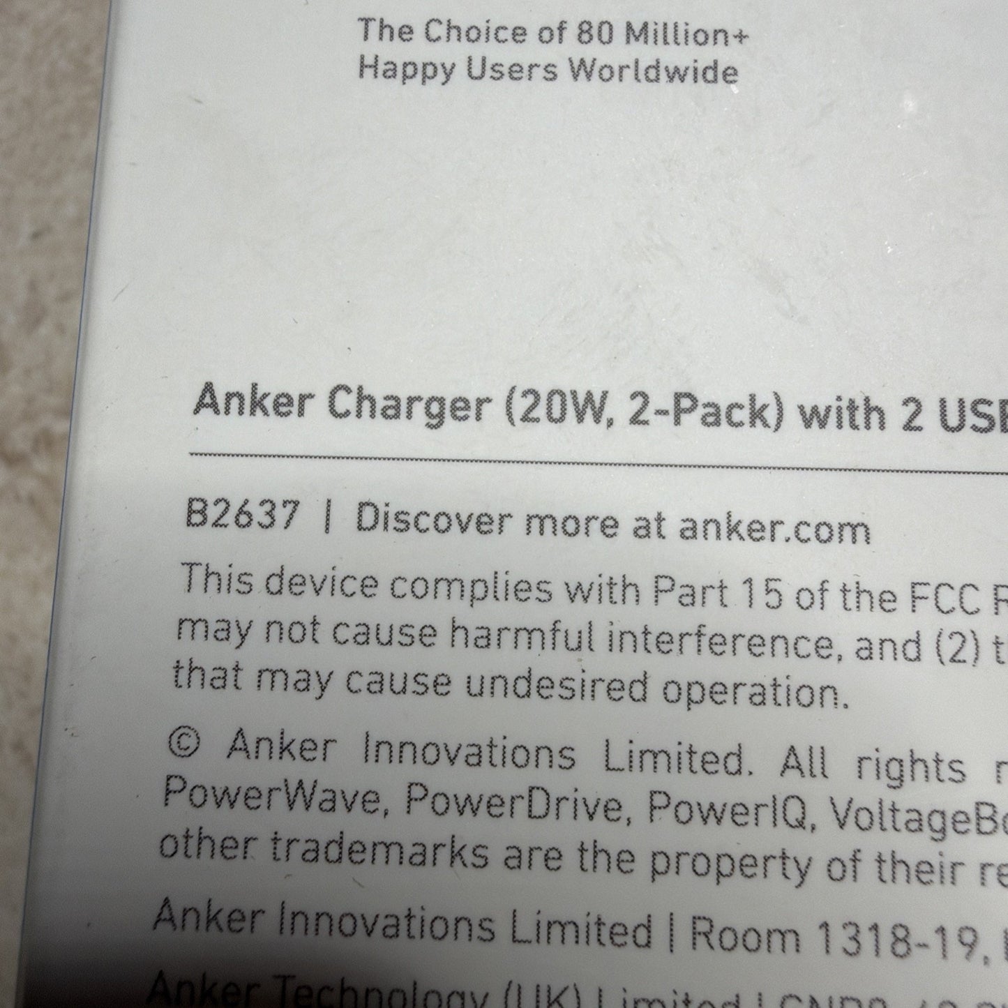 Close-up of product packaging text showing details for an Anker charger 20W 2-pack with 2 USB ports, including compliance with FCC regulations and trademark information.
