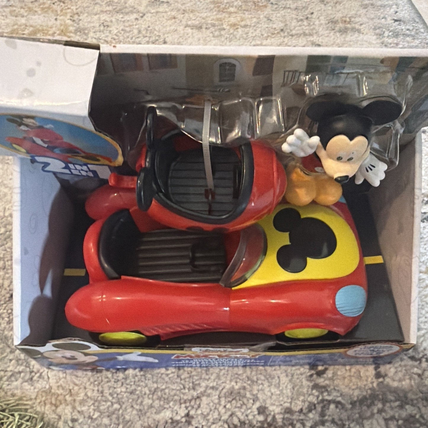Toy set featuring a red and yellow race car with a black Mickey Mouse silhouette on the hood, accompanied by a standing Mickey Mouse figure wearing red shorts and white gloves in packaging.